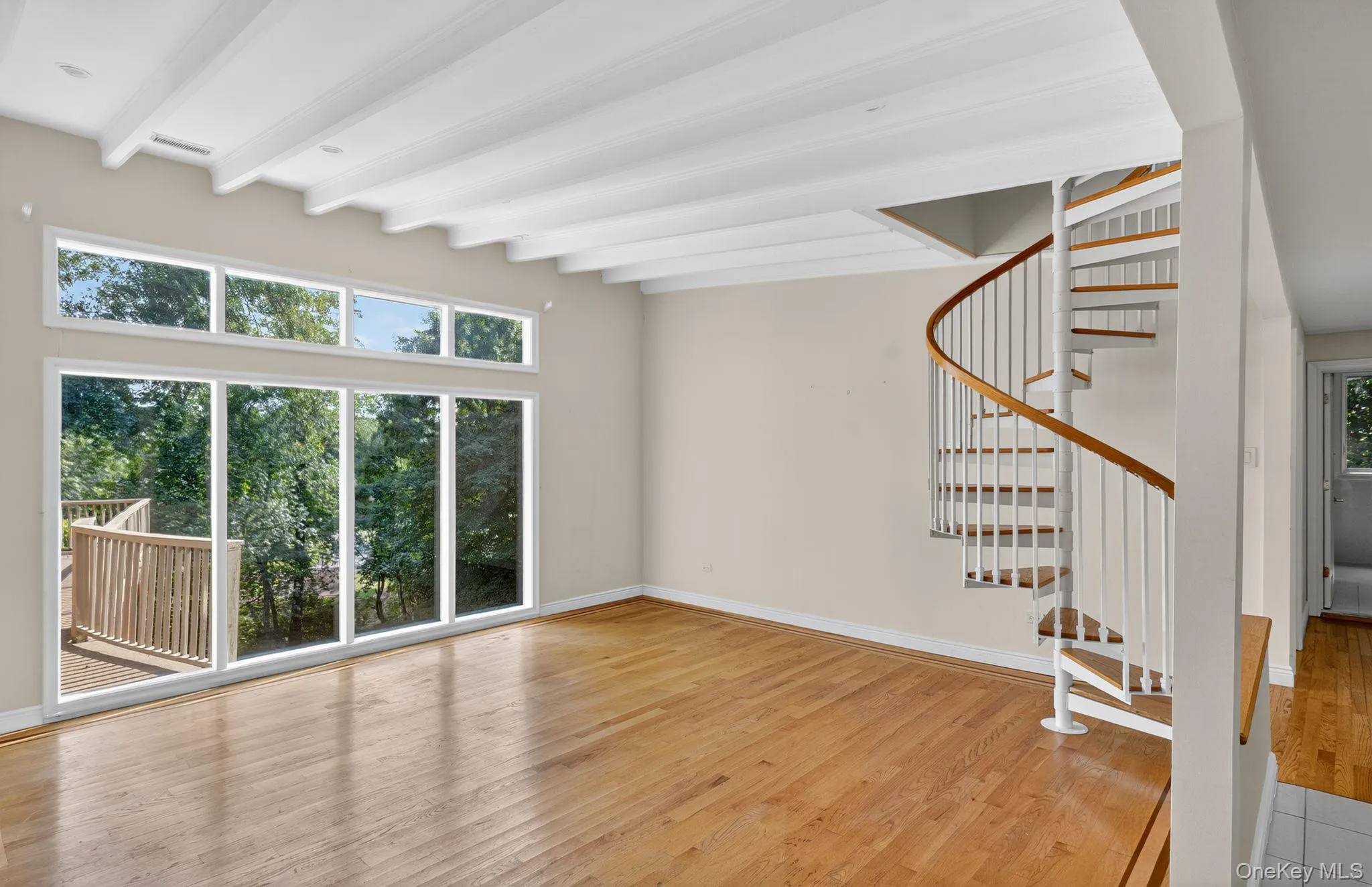 Unfurnished living room with stairs, light wood-style floors, healthy amount of natural light, and beamed ceiling Unfurnished living room with stairs, light wood-style floors, healthy amount of natural light, and beamed ceiling