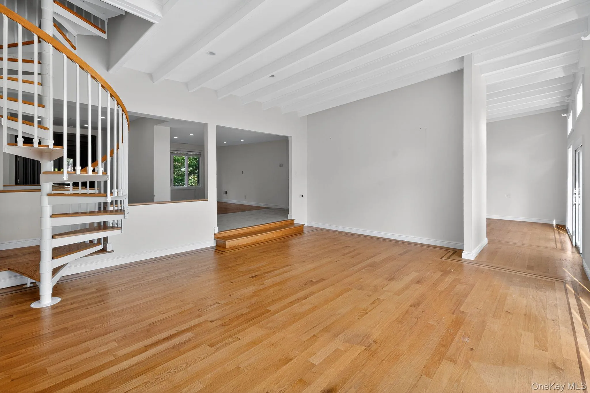 Unfurnished living room featuring beam ceiling, light wood-type flooring, and stairway Unfurnished living room featuring beam ceiling, light wood-type flooring, and stairway