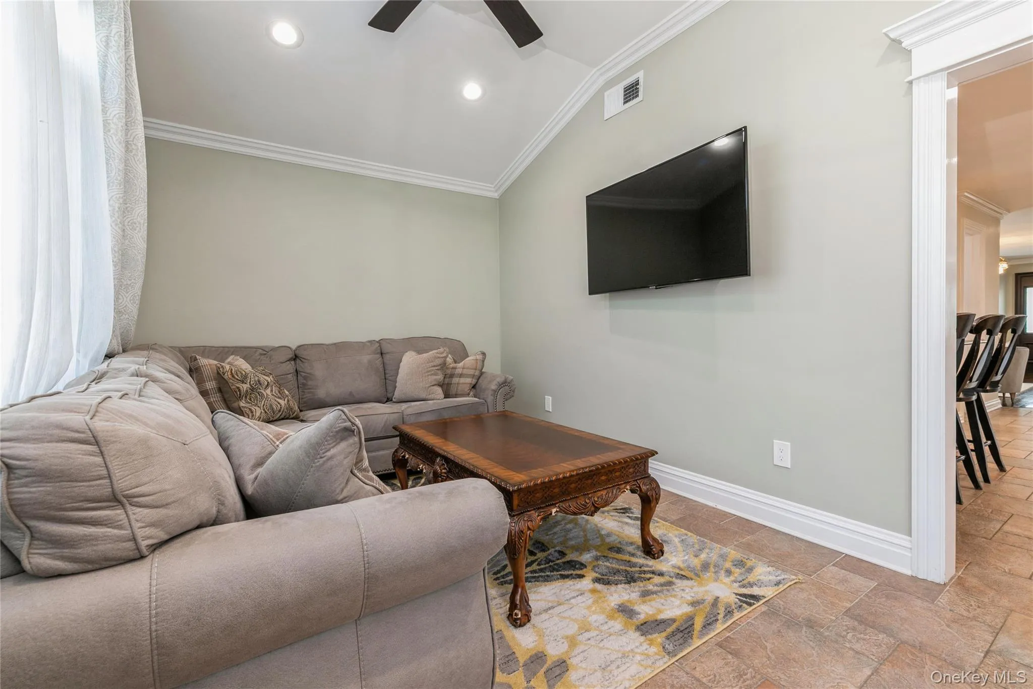Living room with crown molding, ceiling fan, recessed lighting, stone tile floors, and lofted ceiling Living room with crown molding, ceiling fan, recessed lighting, stone tile floors, and lofted ceiling
