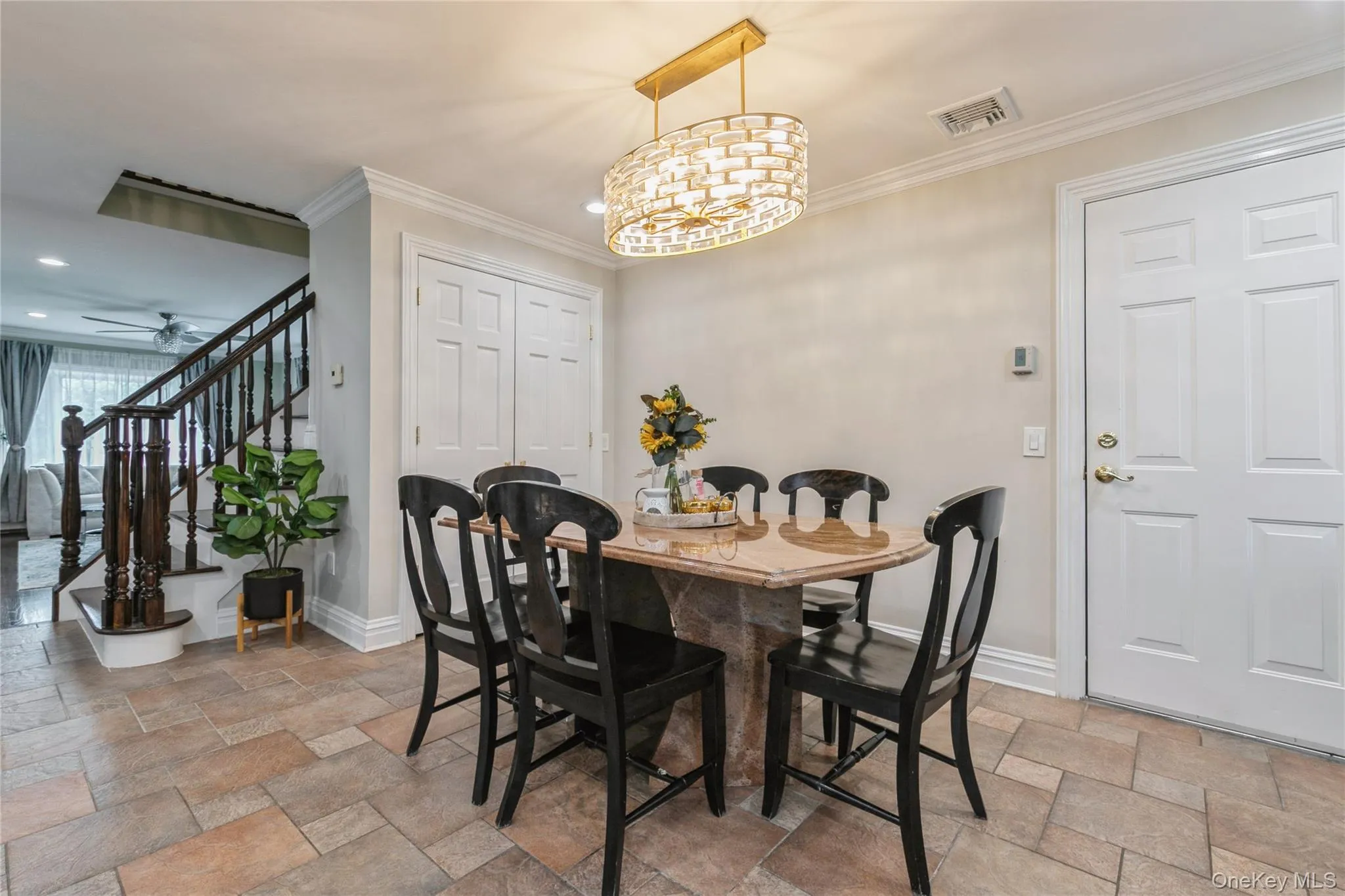 Dining space featuring stone tile flooring, stairs, recessed lighting, a chandelier, and crown molding Dining space featuring stone tile flooring, stairs, recessed lighting, a chandelier, and crown molding
