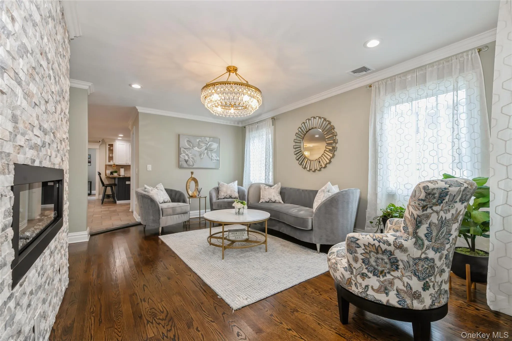 Living room with crown molding, dark wood-style flooring, a chandelier, a stone fireplace, and recessed lighting Living room with crown molding, dark wood-style flooring, a chandelier, a stone fireplace, and recessed lighting