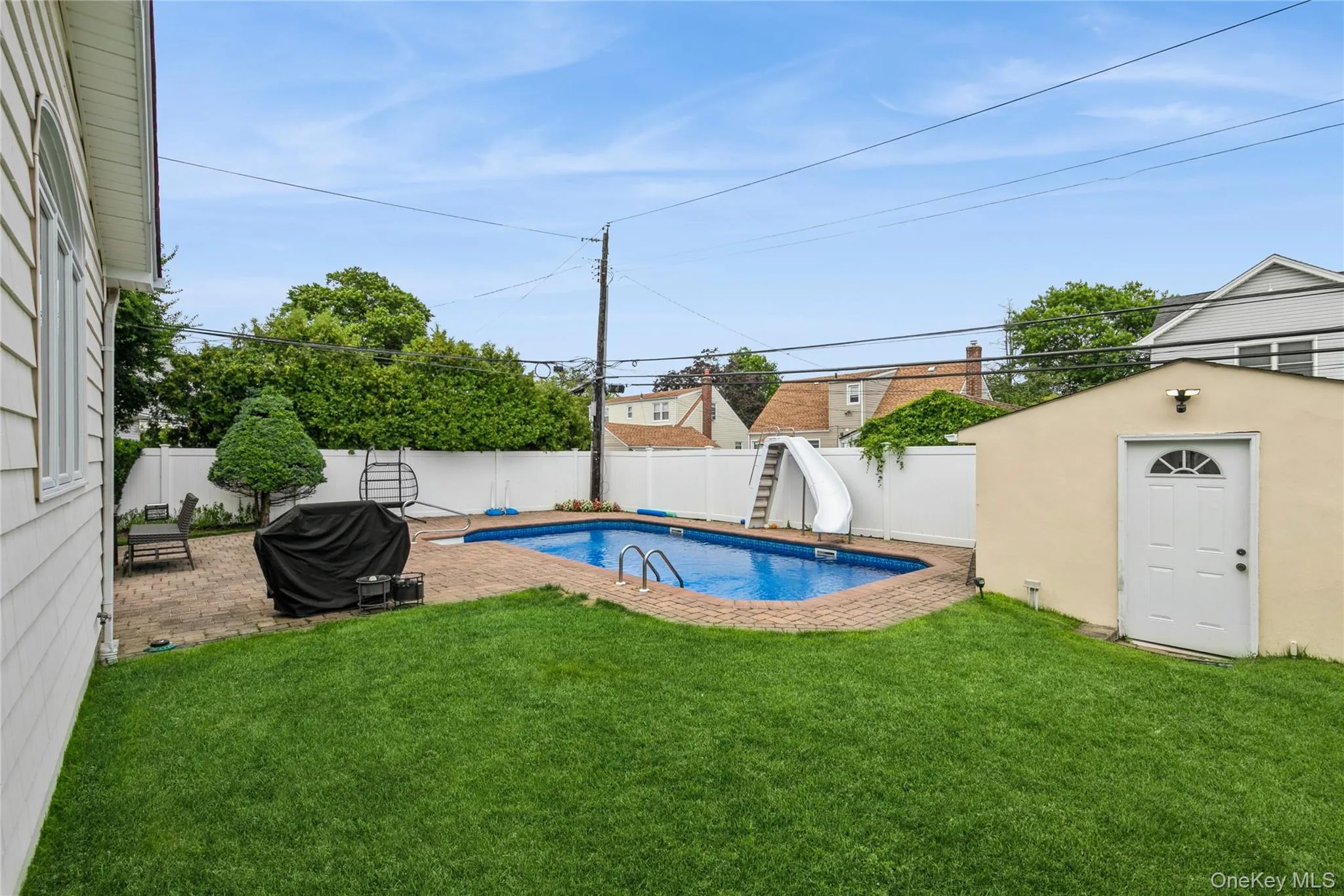View of pool with a water slide, a fenced backyard, an outdoor structure, area for grilling, and a patio area View of pool with a water slide, a fenced backyard, an outdoor structure, area for grilling, and a patio area