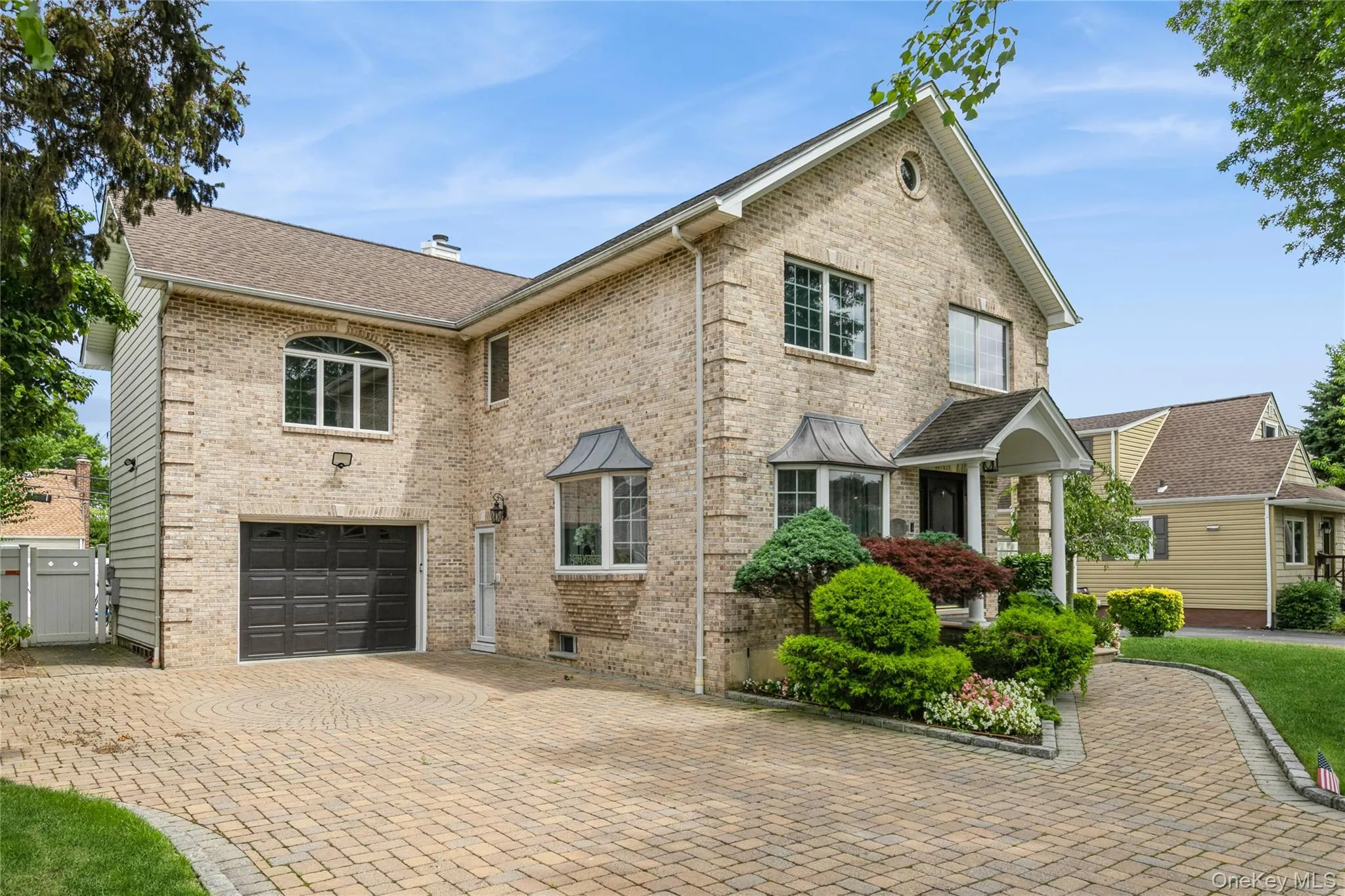 Traditional-style house featuring brick siding, decorative driveway, a shingled roof, and an attached garage Traditional-style house featuring brick siding, decorative driveway, a shingled roof, and an attached garage