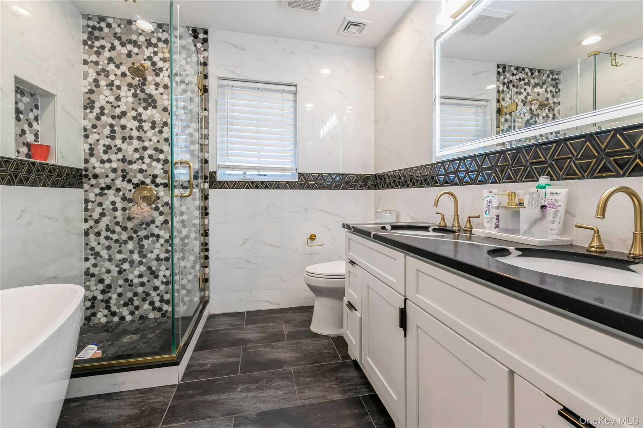Full bathroom with tile walls, a shower stall, a freestanding tub, and double vanity Full bathroom with tile walls, a shower stall, a freestanding tub, and double vanity