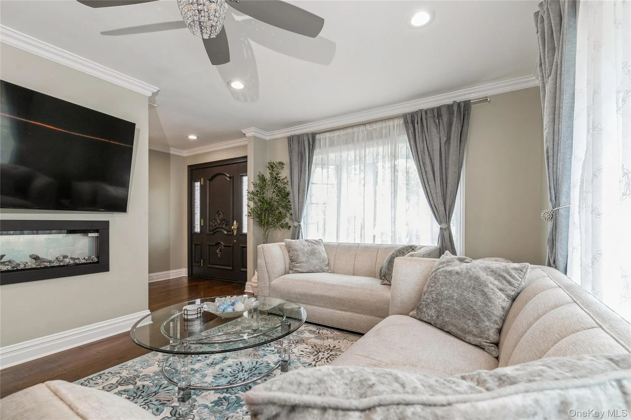 Living room with recessed lighting, a glass covered fireplace, wood finished floors, a ceiling fan, and ornamental molding Living room with recessed lighting, a glass covered fireplace, wood finished floors, a ceiling fan, and ornamental molding