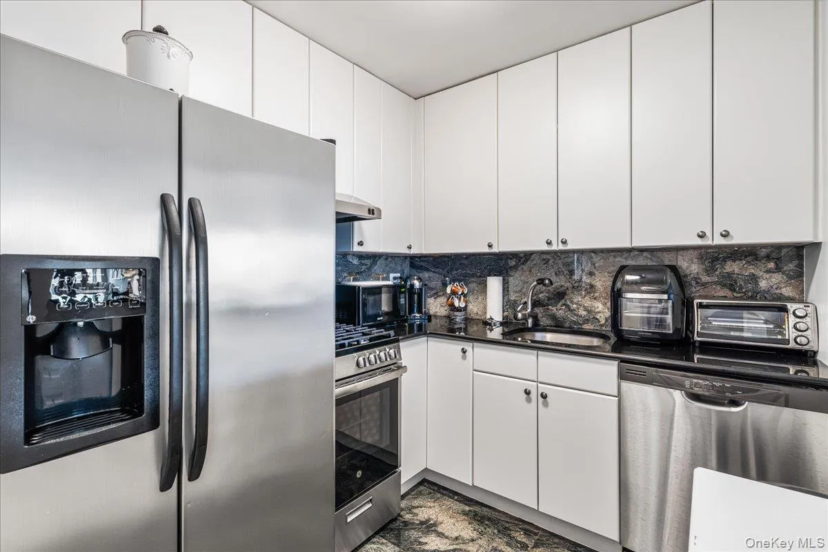 Kitchen with stainless steel appliances, dark countertops, tasteful backsplash, and white cabinets Kitchen with stainless steel appliances, dark countertops, tasteful backsplash, and white cabinets