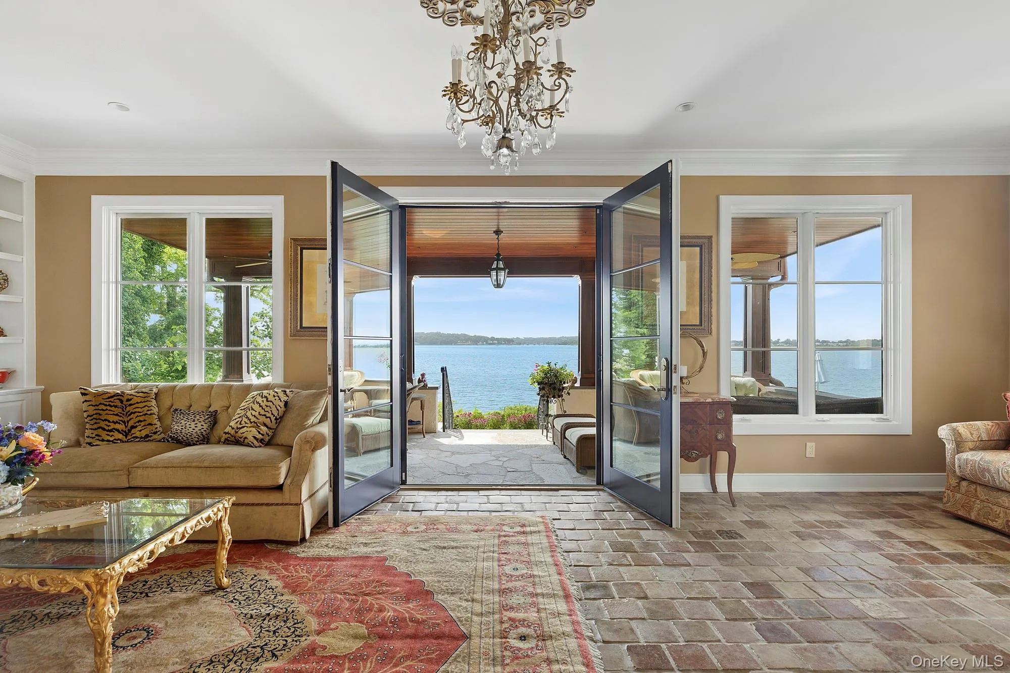 Doorway to outside with plenty of natural light, brick flooring, ornamental molding, a water view, and a chandelier Doorway to outside with plenty of natural light, brick flooring, ornamental molding, a water view, and a chandelier