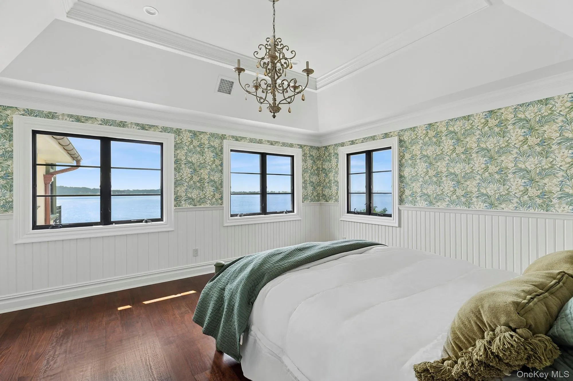 Bedroom with wallpapered walls, a tray ceiling, dark wood finished floors, wainscoting, and crown molding Bedroom with wallpapered walls, a tray ceiling, dark wood finished floors, wainscoting, and crown molding