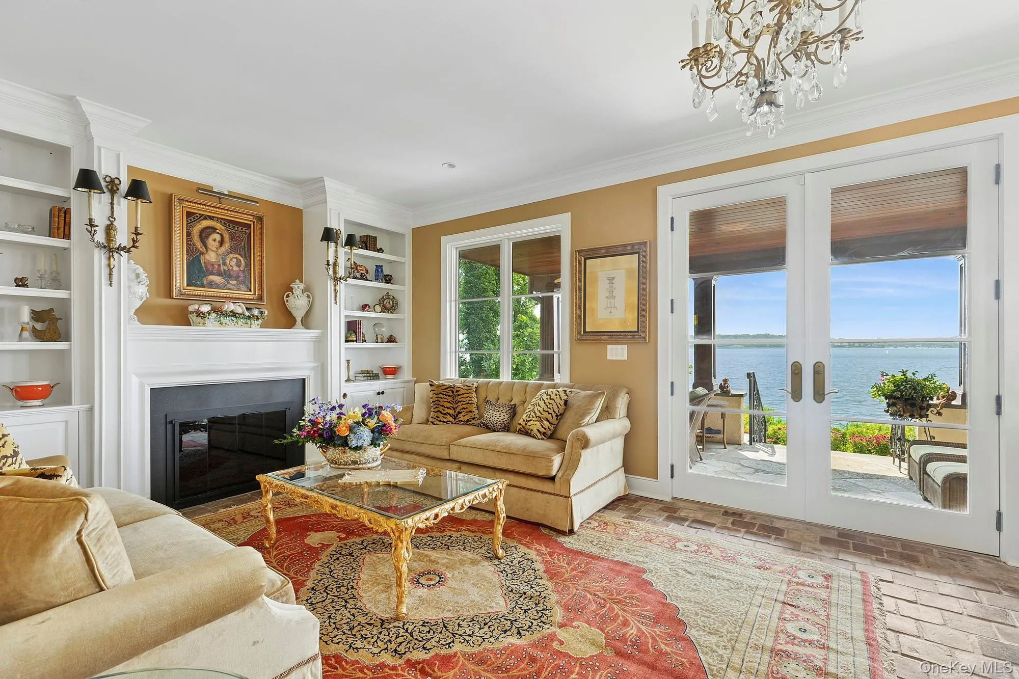 Living area with a glass covered fireplace, ornamental molding, a water view, french doors, and a chandelier Living area with a glass covered fireplace, ornamental molding, a water view, french doors, and a chandelier