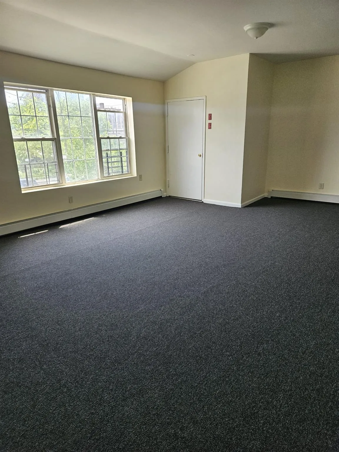 Unfurnished room with a baseboard heating unit, lofted ceiling, and dark colored carpet Unfurnished room with a baseboard heating unit, lofted ceiling, and dark colored carpet
