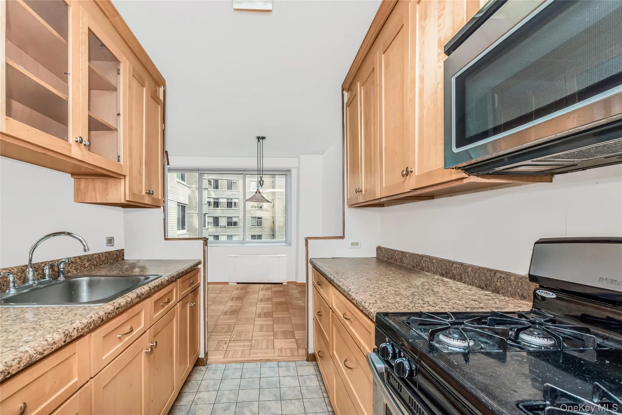 Kitchen with range with gas stovetop, stainless steel microwave, light brown cabinets, glass insert cabinets, and decorative light fixtures Kitchen with range with gas stovetop, stainless steel microwave, light brown cabinets, glass insert cabinets, and decorative light fixtures
