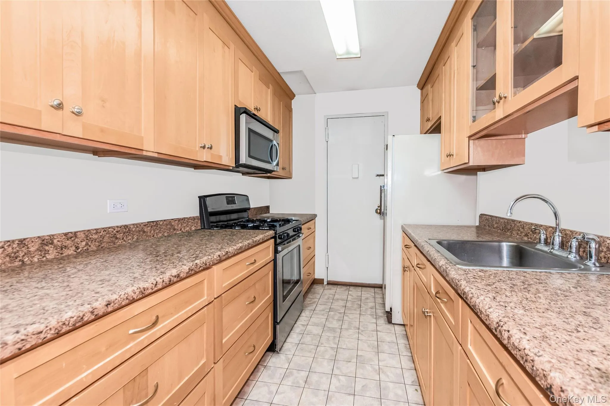 Kitchen with light brown cabinetry, appliances with stainless steel finishes, and glass insert cabinets Kitchen with light brown cabinetry, appliances with stainless steel finishes, and glass insert cabinets