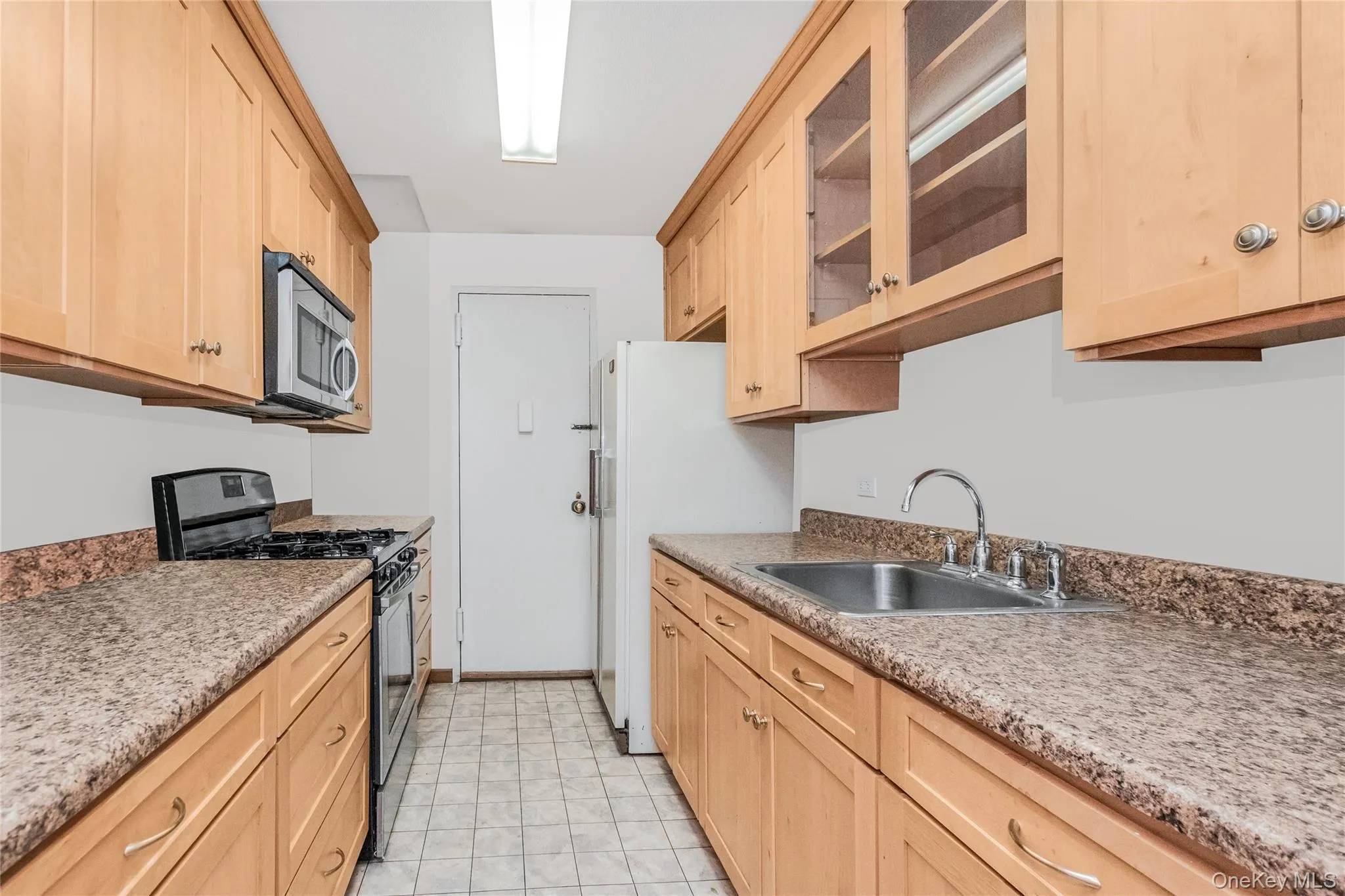 Kitchen featuring light brown cabinetry, appliances with stainless steel finishes, glass insert cabinets, and light countertops Kitchen featuring light brown cabinetry, appliances with stainless steel finishes, glass insert cabinets, and light countertops
