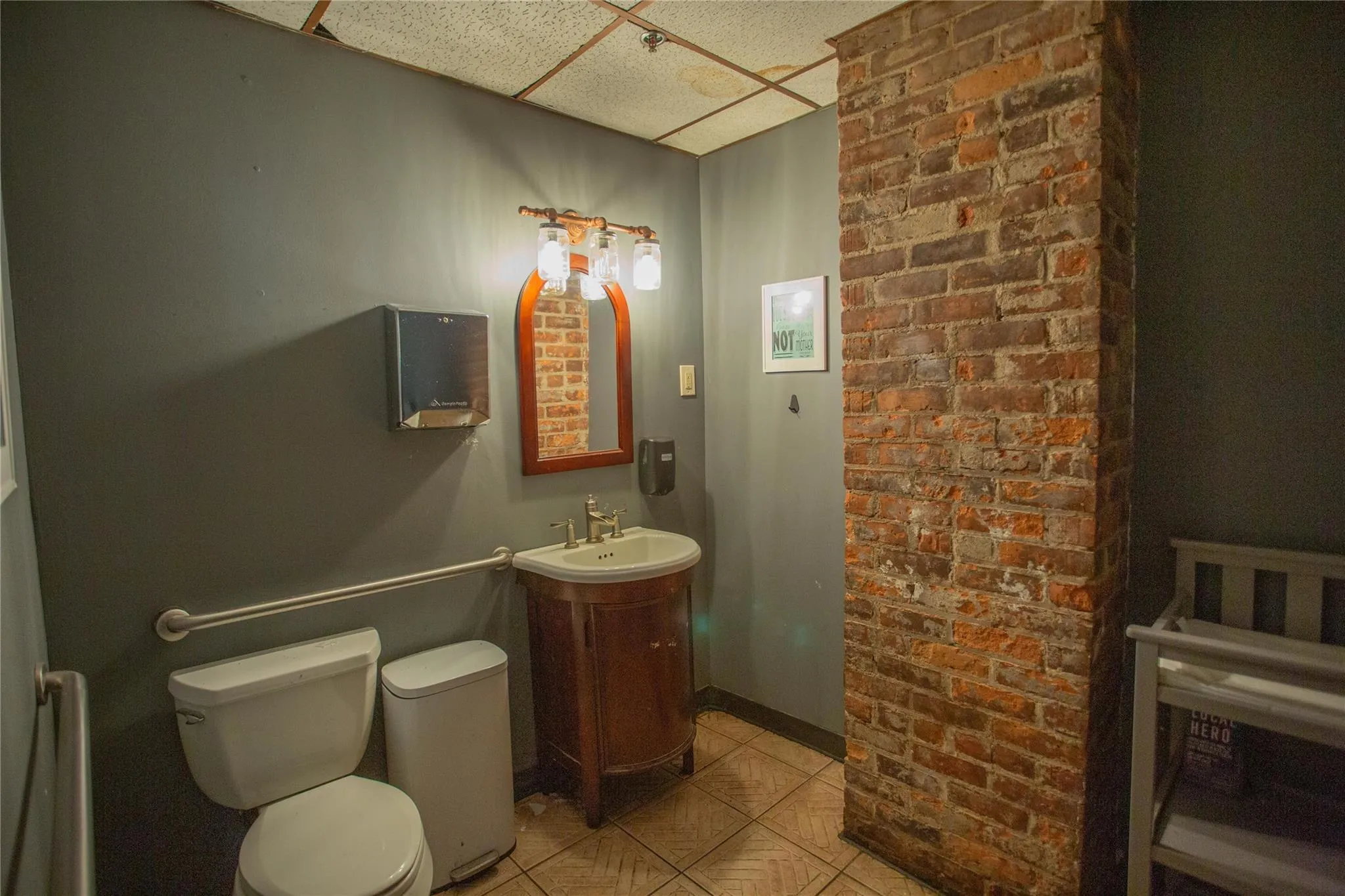 Bathroom featuring a paneled ceiling, vanity, tile patterned flooring, and brick wall Bathroom featuring a paneled ceiling, vanity, tile patterned flooring, and brick wall