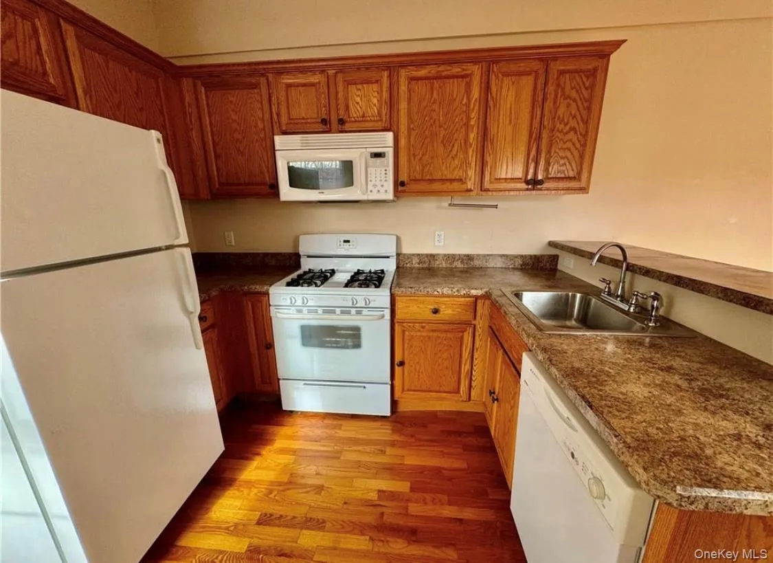Kitchen with white appliances, brown cabinets, light wood-style floors, and dark countertops Kitchen with white appliances, brown cabinets, light wood-style floors, and dark countertops