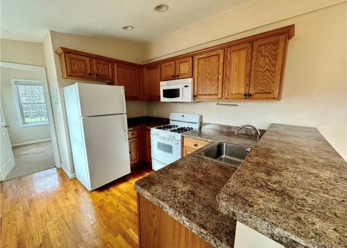 Kitchen featuring white appliances, brown cabinets, light wood-style floors, dark countertops, and recessed lighting Kitchen featuring white appliances, brown cabinets, light wood-style floors, dark countertops, and recessed lighting