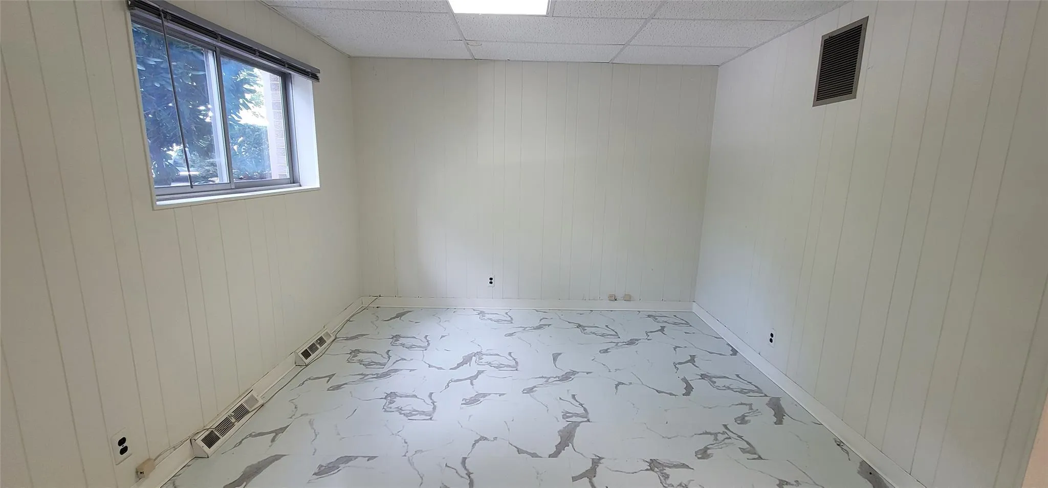 Unfurnished room with wood walls and a drop ceiling Unfurnished room with wood walls and a drop ceiling