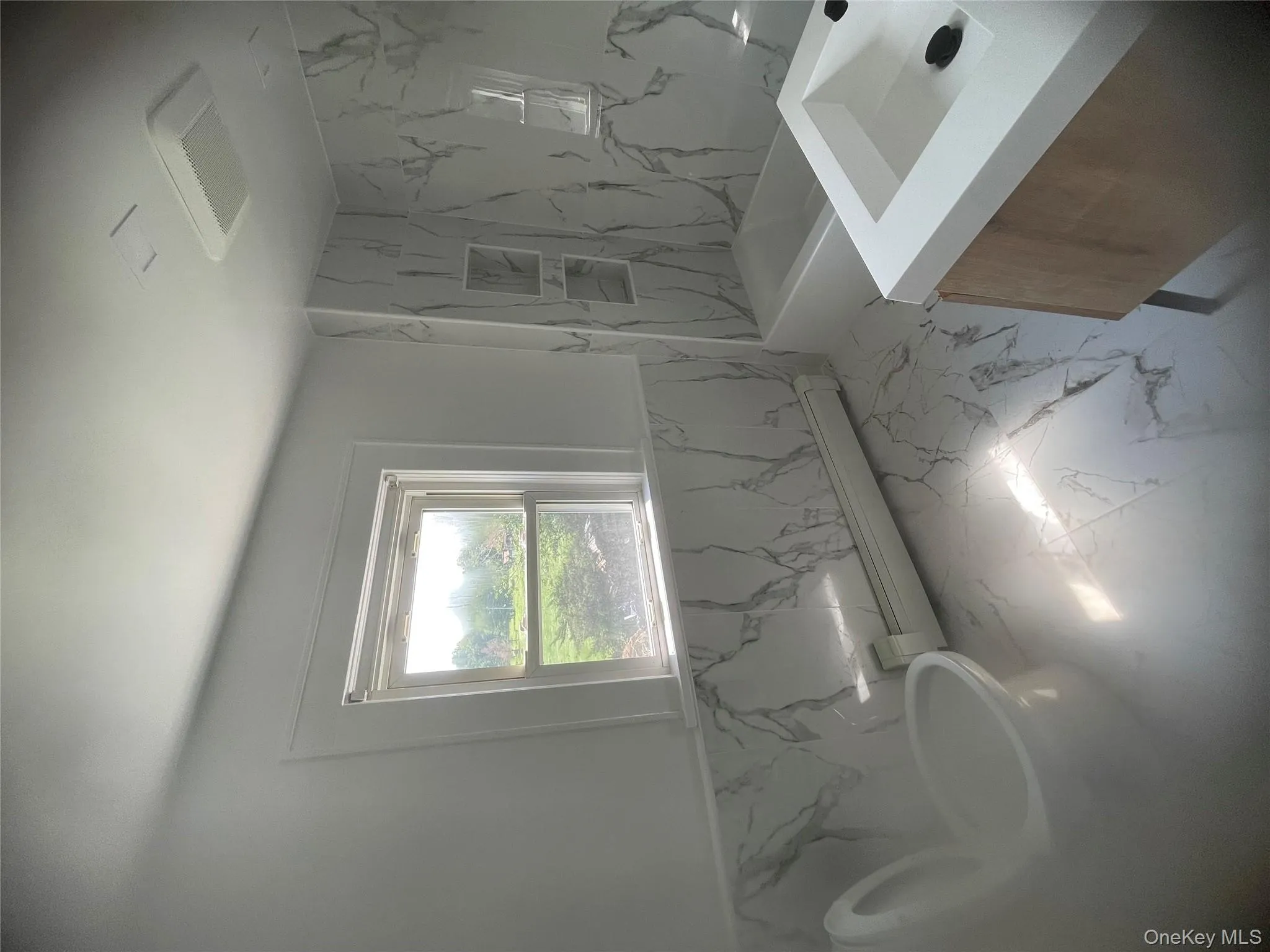 Full bath featuring a baseboard heating unit, vanity, marble finish flooring, a wainscoted wall, and tile walls Full bath featuring a baseboard heating unit, vanity, marble finish flooring, a wainscoted wall, and tile walls