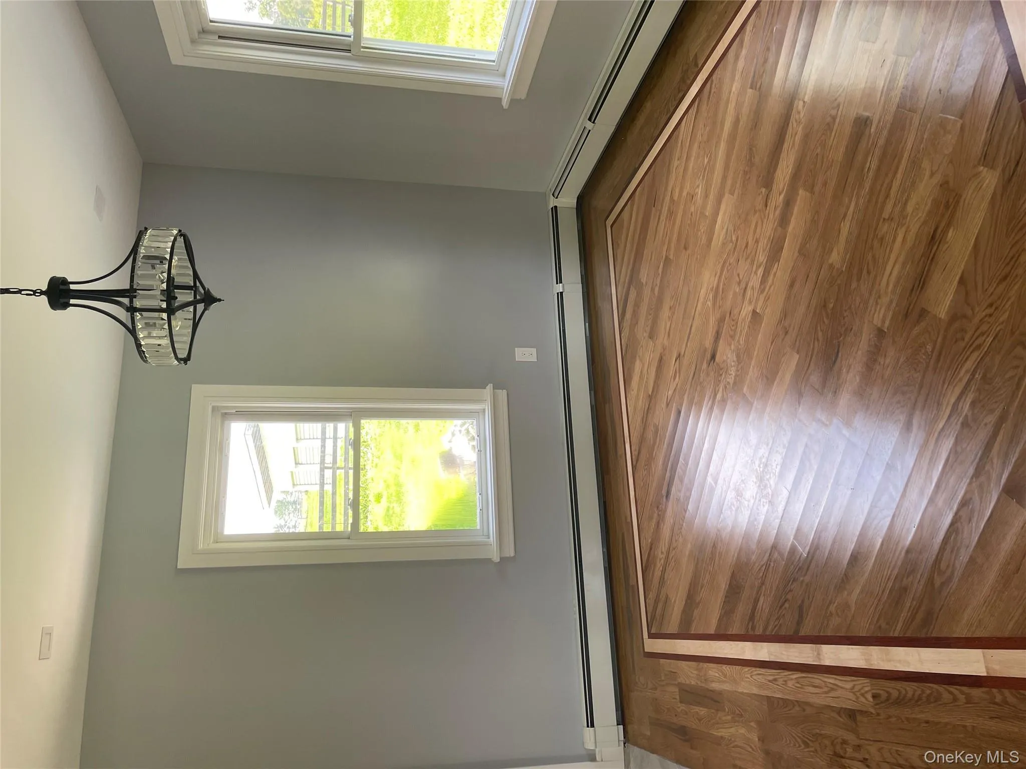 Unfurnished room featuring wood finished floors, baseboard heating, and a chandelier Unfurnished room featuring wood finished floors, baseboard heating, and a chandelier