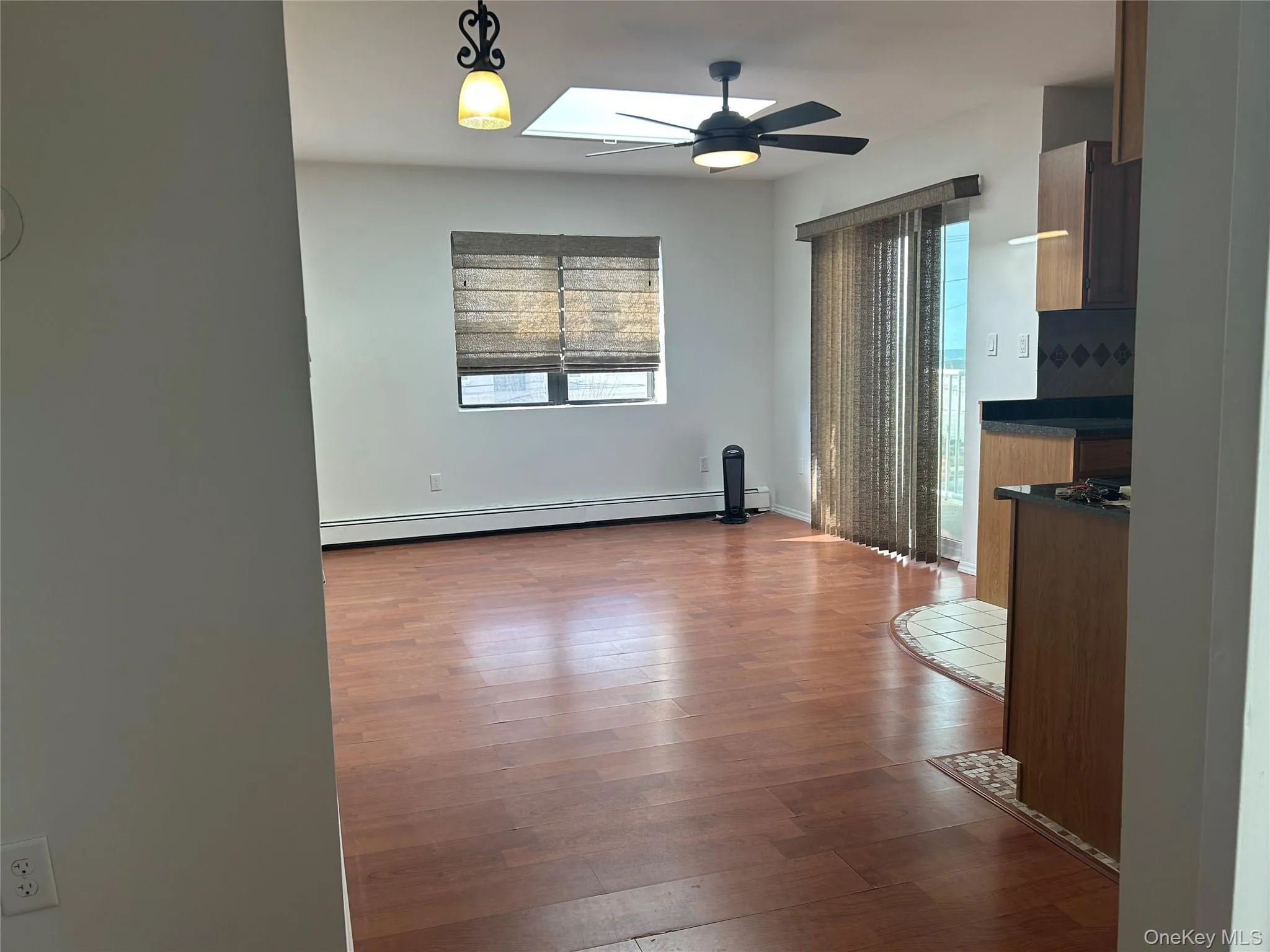 Spare room featuring dark wood-style floors, a ceiling fan, baseboard heating, and a skylight Spare room featuring dark wood-style floors, a ceiling fan, baseboard heating, and a skylight