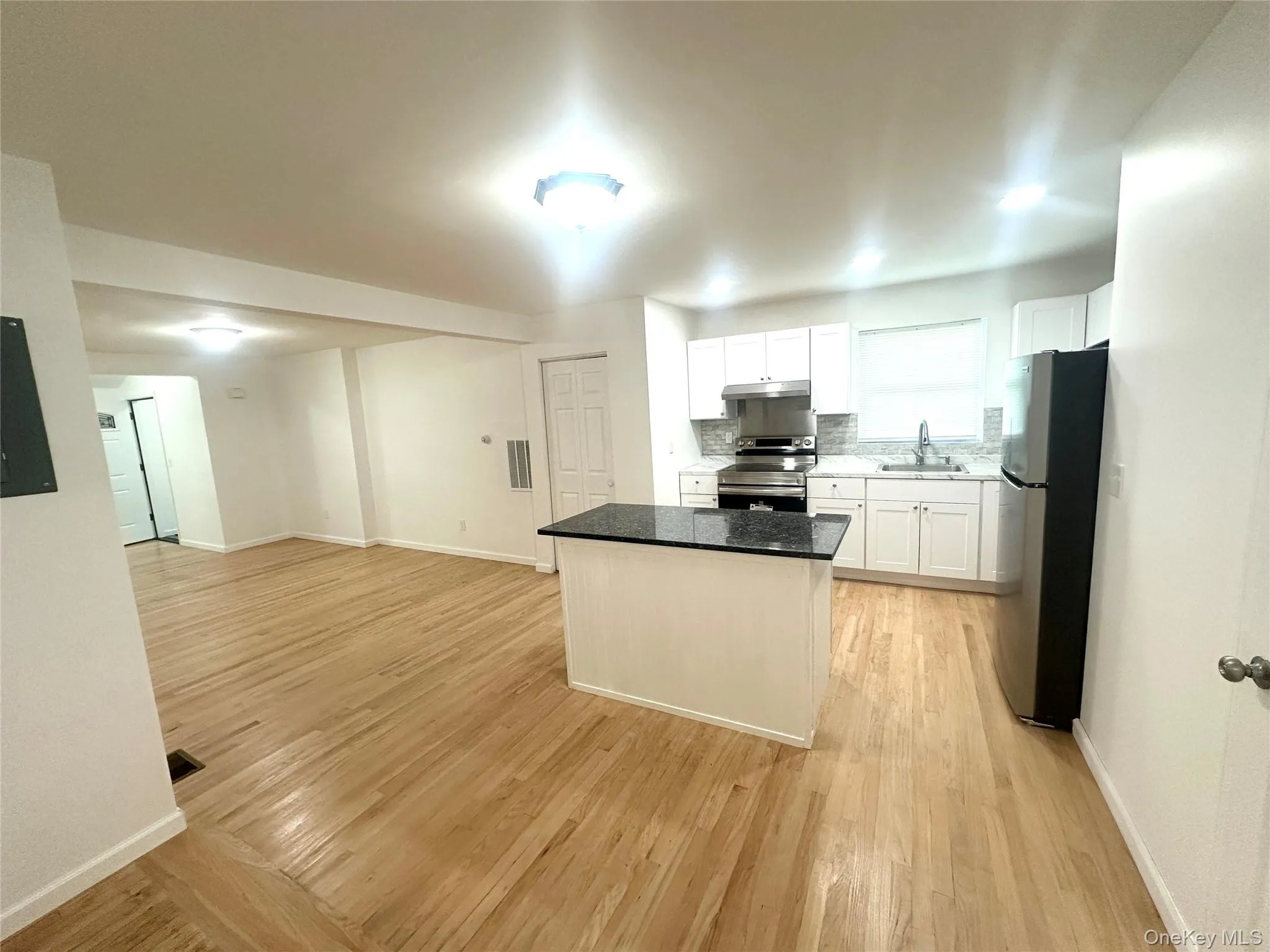 Kitchen featuring stainless steel appliances, light wood finished floors, a kitchen island, white cabinets, and open floor plan Kitchen featuring stainless steel appliances, light wood finished floors, a kitchen island, white cabinets, and open floor plan