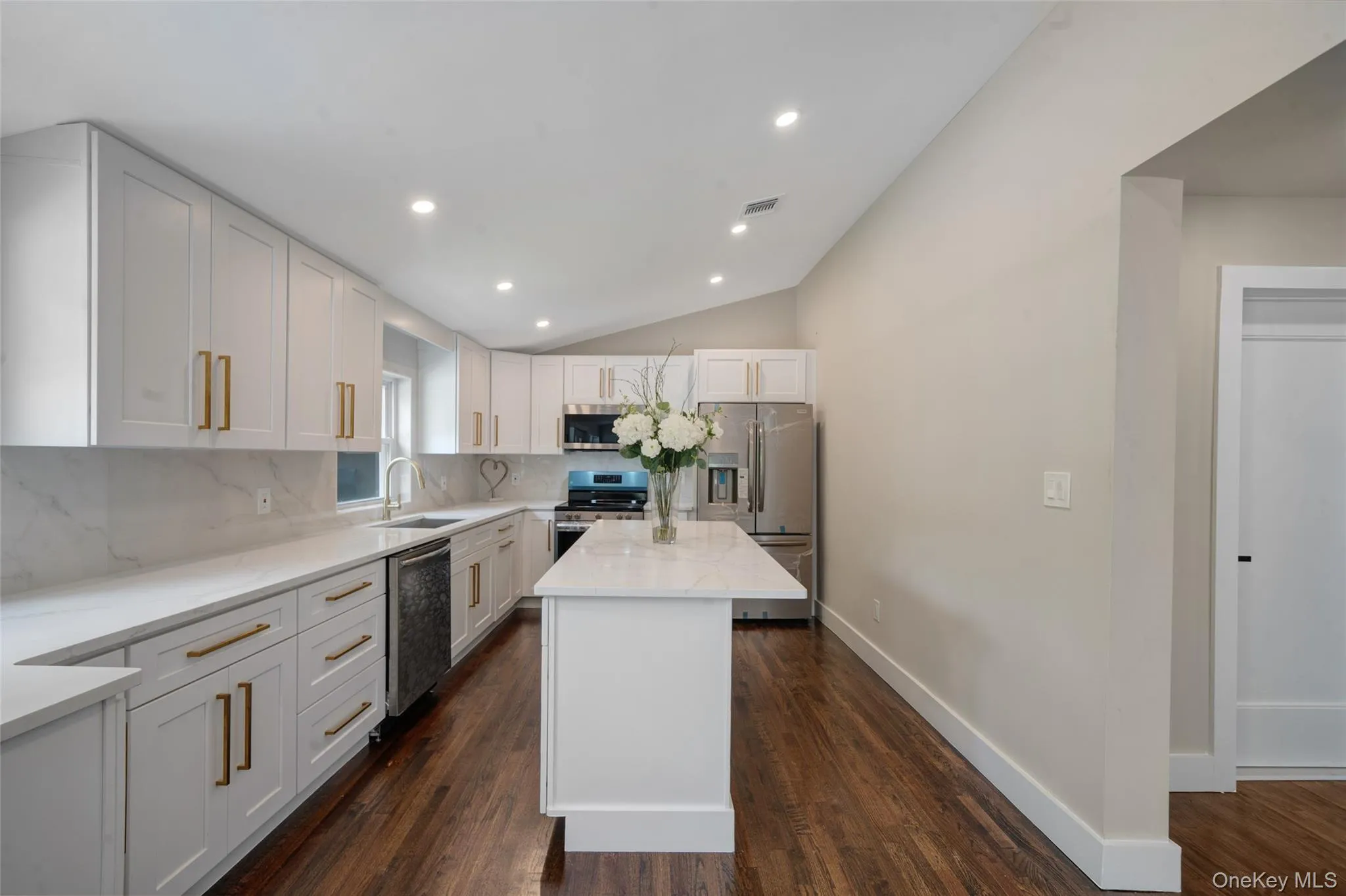 Kitchen with appliances with stainless steel finishes, tasteful backsplash, lofted ceiling, dark wood-style flooring, and white cabinetry Kitchen with appliances with stainless steel finishes, tasteful backsplash, lofted ceiling, dark wood-style flooring, and white cabinetry