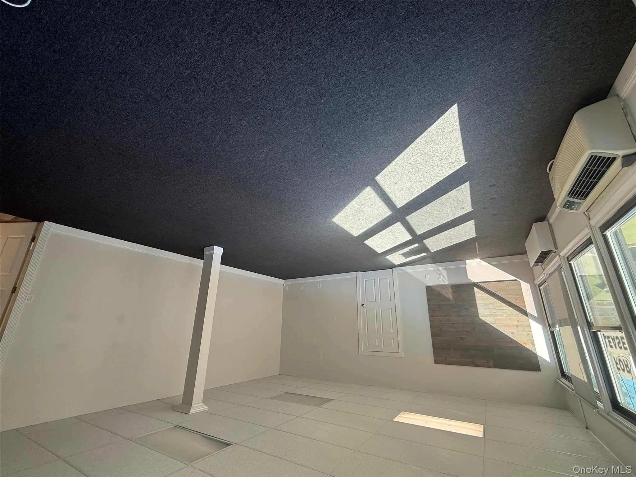 Basement with a paneled ceiling, dark carpet, and an AC wall unit Basement with a paneled ceiling, dark carpet, and an AC wall unit