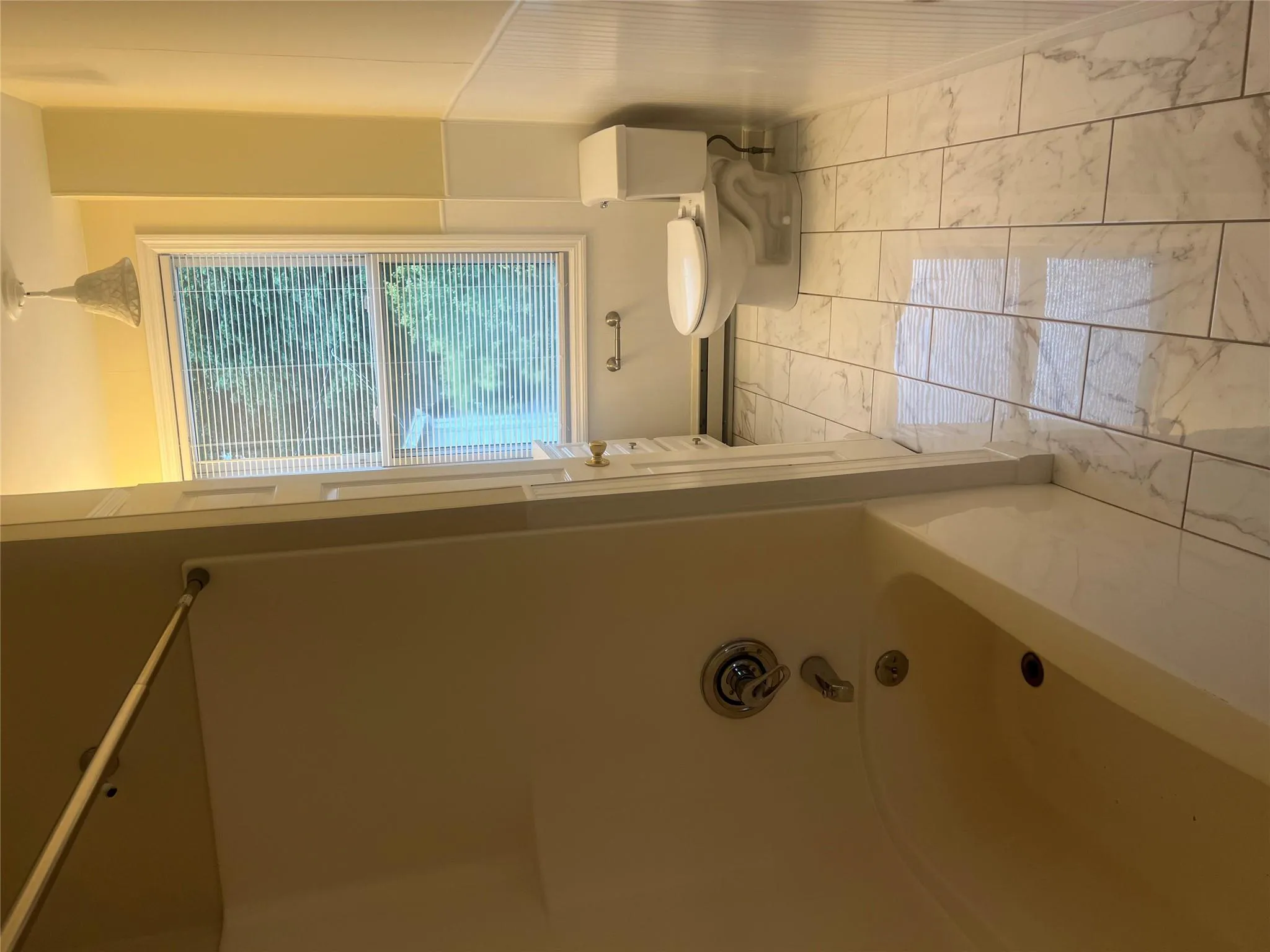 Bathroom with marble finish flooring, tub / shower combination, a baseboard radiator, and a wainscoted wall Bathroom with marble finish flooring, tub / shower combination, a baseboard radiator, and a wainscoted wall