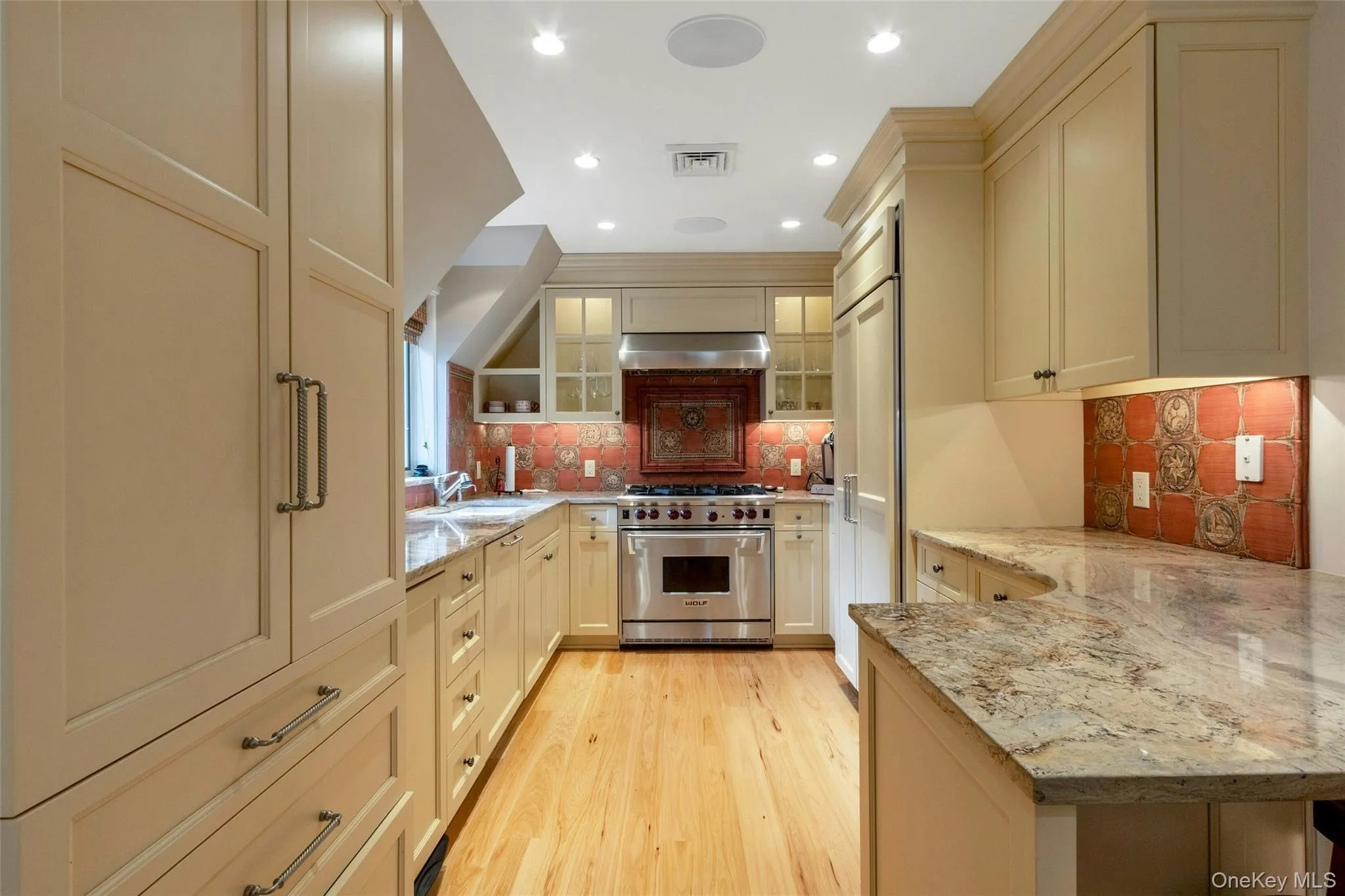 Kitchen with high end appliances, a peninsula, light wood finished floors, glass insert cabinets, and light stone counters Kitchen with high end appliances, a peninsula, light wood finished floors, glass insert cabinets, and light stone counters