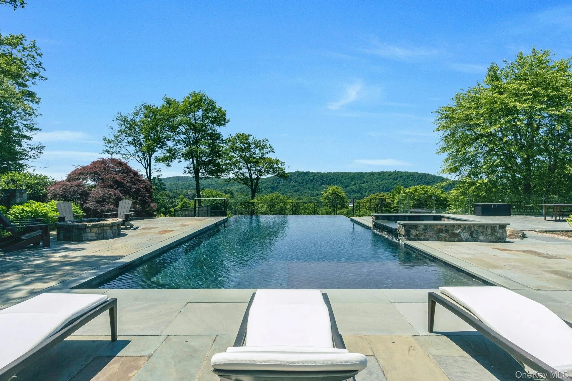 View of pool featuring a pool with connected hot tub, a forest view, a patio area, and a fire pit View of pool featuring a pool with connected hot tub, a forest view, a patio area, and a fire pit