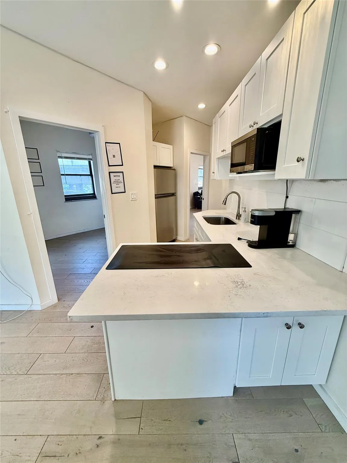 Kitchen with a peninsula, light wood-type flooring, white cabinets, freestanding refrigerator, and recessed lighting Kitchen with a peninsula, light wood-type flooring, white cabinets, freestanding refrigerator, and recessed lighting