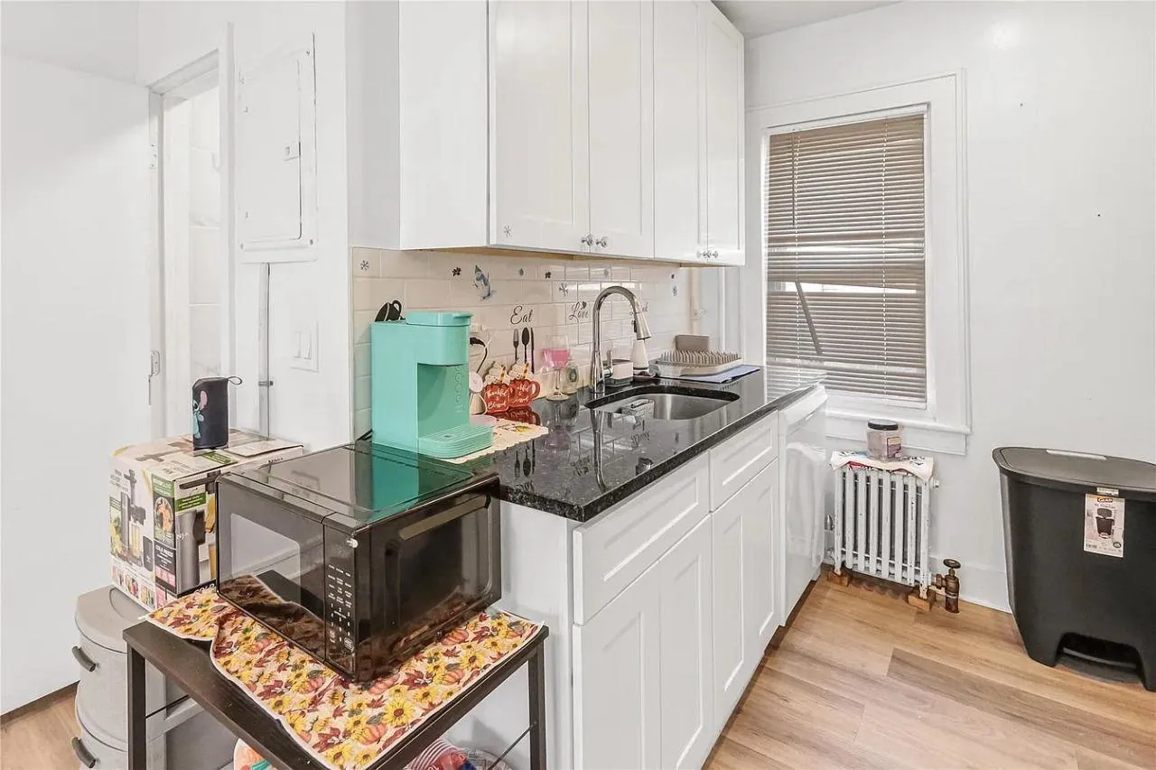 Kitchen with black microwave, light wood-type flooring, radiator, dark stone countertops, and tasteful backsplash Kitchen with black microwave, light wood-type flooring, radiator, dark stone countertops, and tasteful backsplash