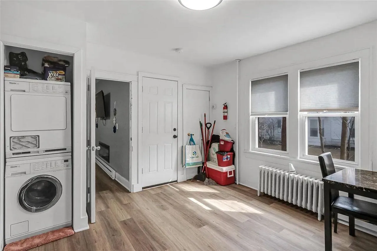 Laundry area featuring stacked washer and clothes dryer, wood finished floors, and radiator Laundry area featuring stacked washer and clothes dryer, wood finished floors, and radiator