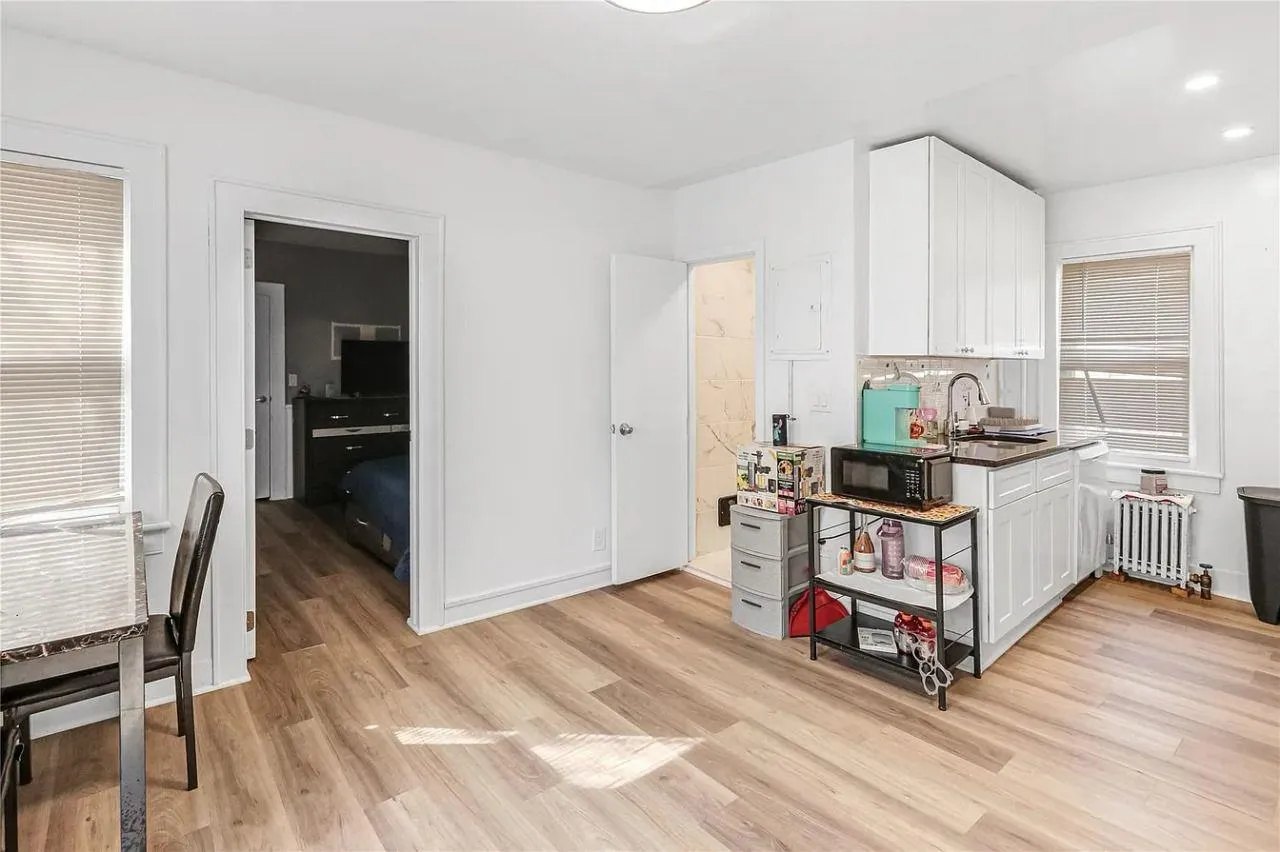 Kitchen featuring light wood-type flooring, white cabinetry, radiator heating unit, black microwave, and recessed lighting Kitchen featuring light wood-type flooring, white cabinetry, radiator heating unit, black microwave, and recessed lighting