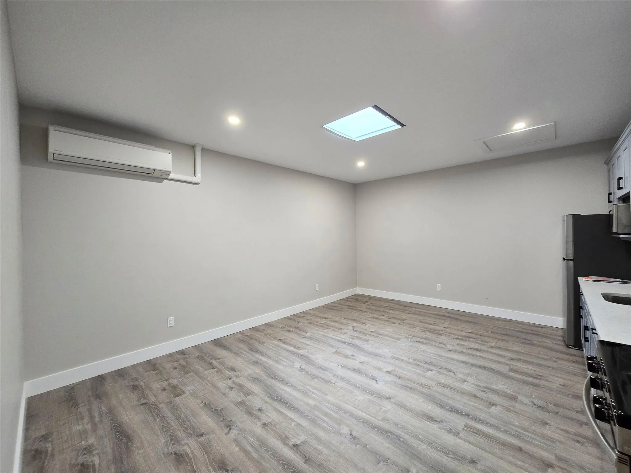 Kitchen featuring light wood-type flooring, a wall mounted air conditioner, recessed lighting, and freestanding refrigerator Kitchen featuring light wood-type flooring, a wall mounted air conditioner, recessed lighting, and freestanding refrigerator