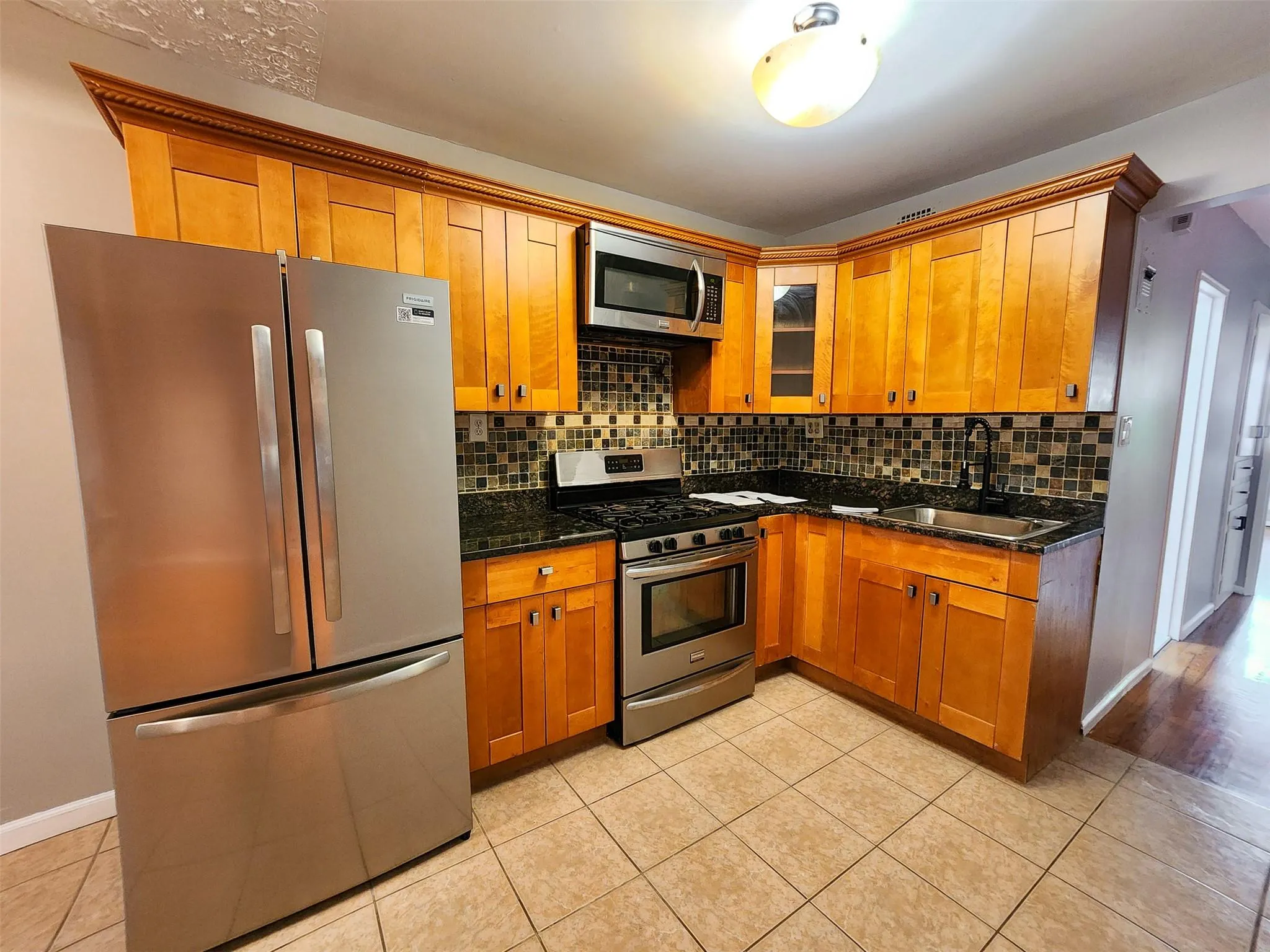 Kitchen featuring stainless steel appliances, backsplash, light tile patterned flooring, and brown cabinets Kitchen featuring stainless steel appliances, backsplash, light tile patterned flooring, and brown cabinets