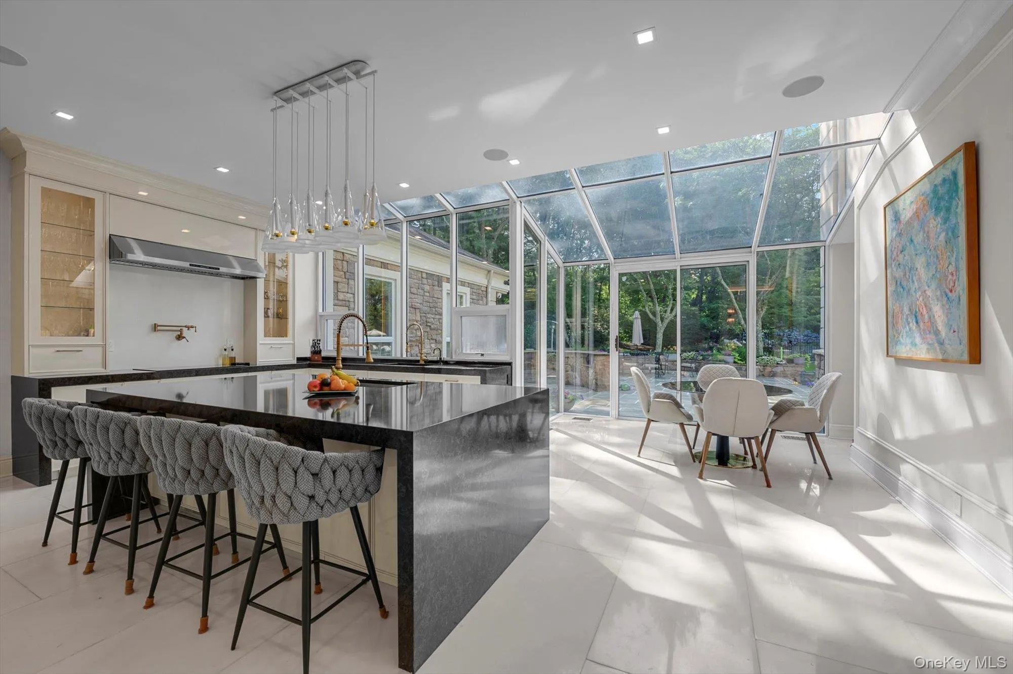 Kitchen with a sunroom, floor to ceiling windows, a spacious island, glass insert cabinets, and wall chimney exhaust hood Kitchen with a sunroom, floor to ceiling windows, a spacious island, glass insert cabinets, and wall chimney exhaust hood