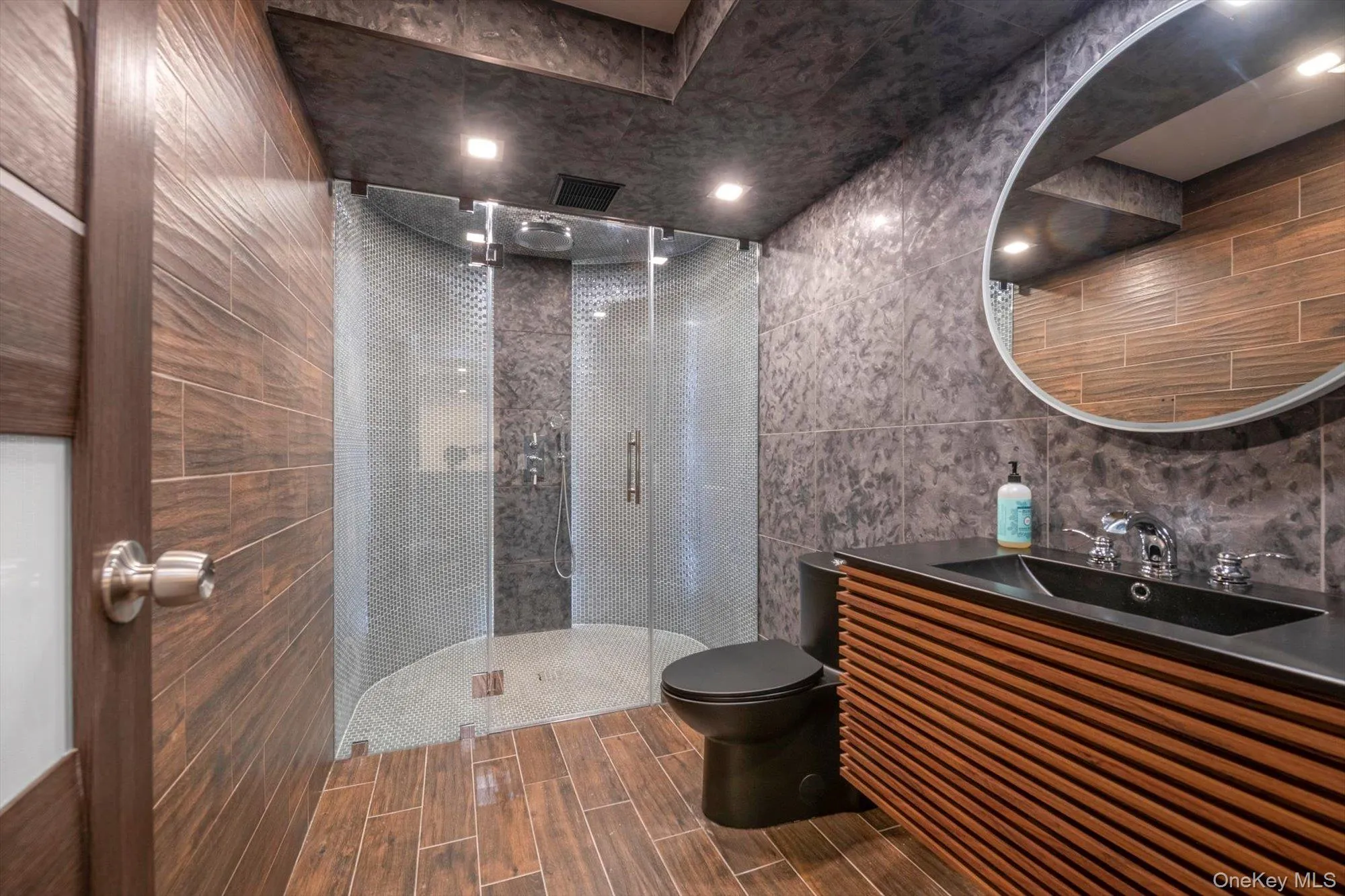 Full bathroom with tile walls, a shower stall, vanity, wood tiled floors, and backsplash Full bathroom with tile walls, a shower stall, vanity, wood tiled floors, and backsplash