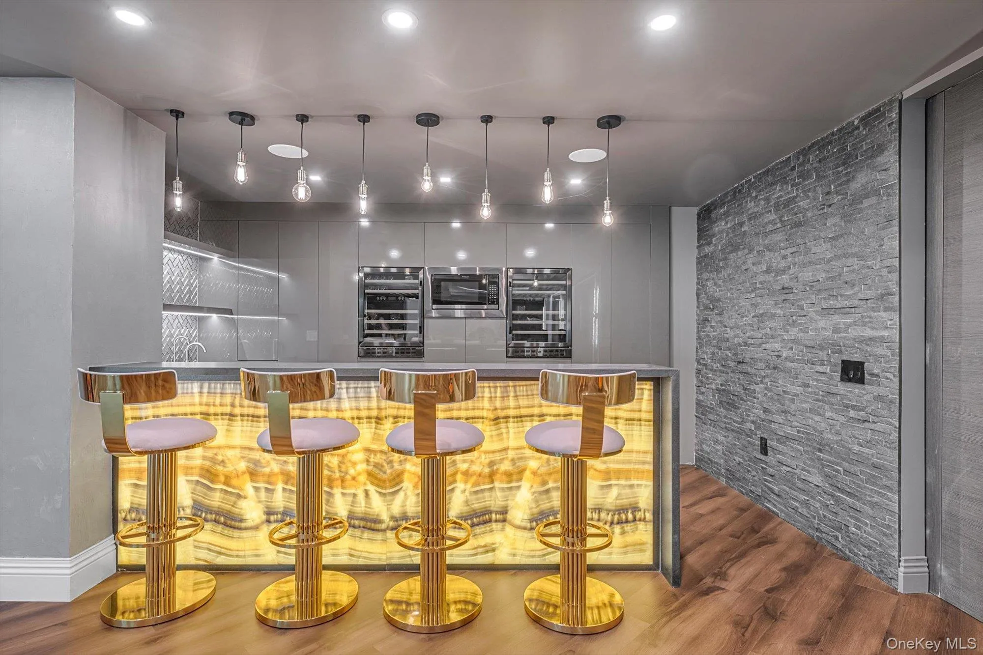 Community bar area featuring beverage cooler, wood finished floors, stainless steel microwave, recessed lighting, and hanging light fixtures Community bar area featuring beverage cooler, wood finished floors, stainless steel microwave, recessed lighting, and hanging light fixtures