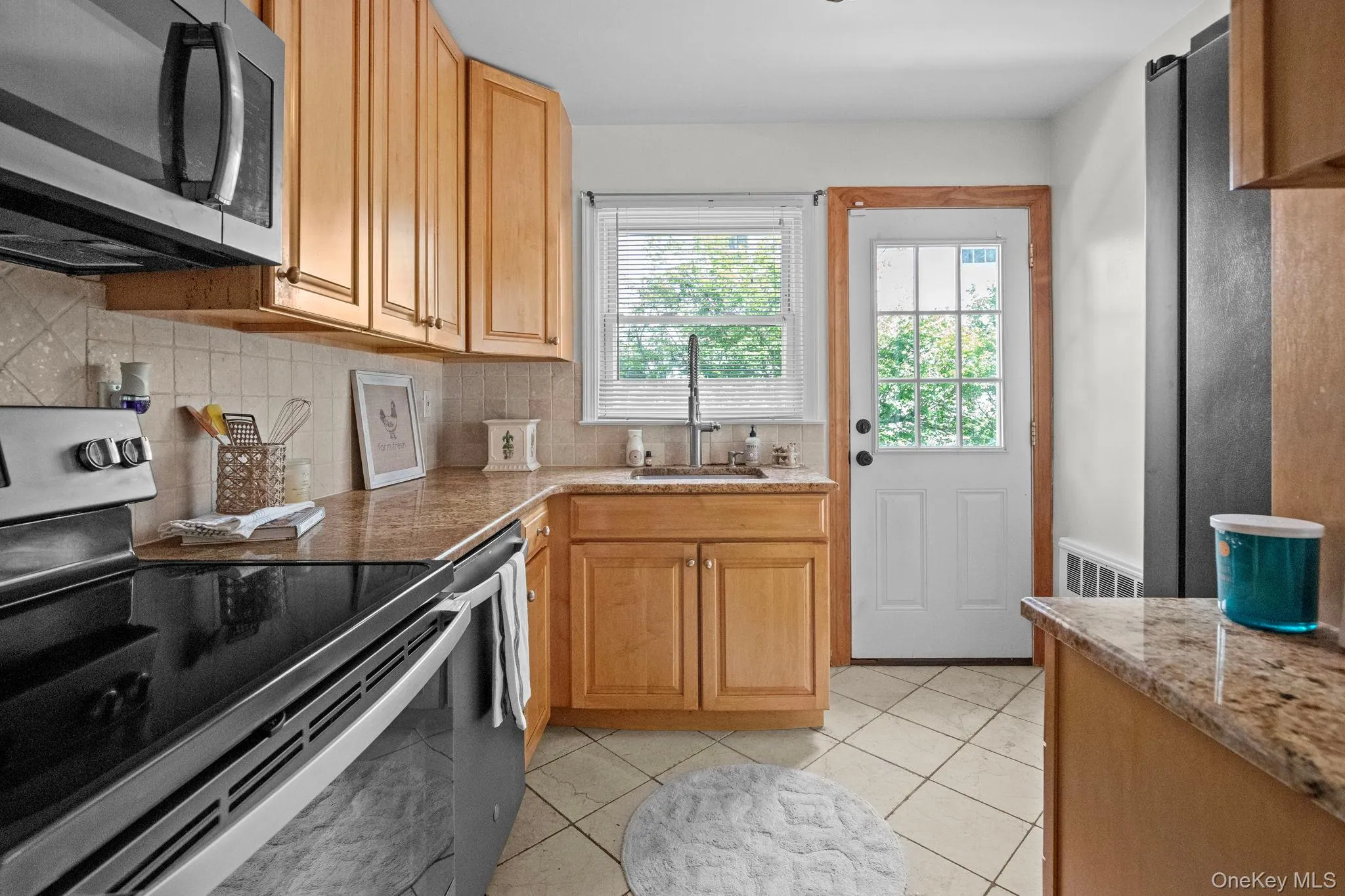 Kitchen with appliances with stainless steel finishes, light tile patterned floors, decorative backsplash, and light stone counters Kitchen with appliances with stainless steel finishes, light tile patterned floors, decorative backsplash, and light stone counters