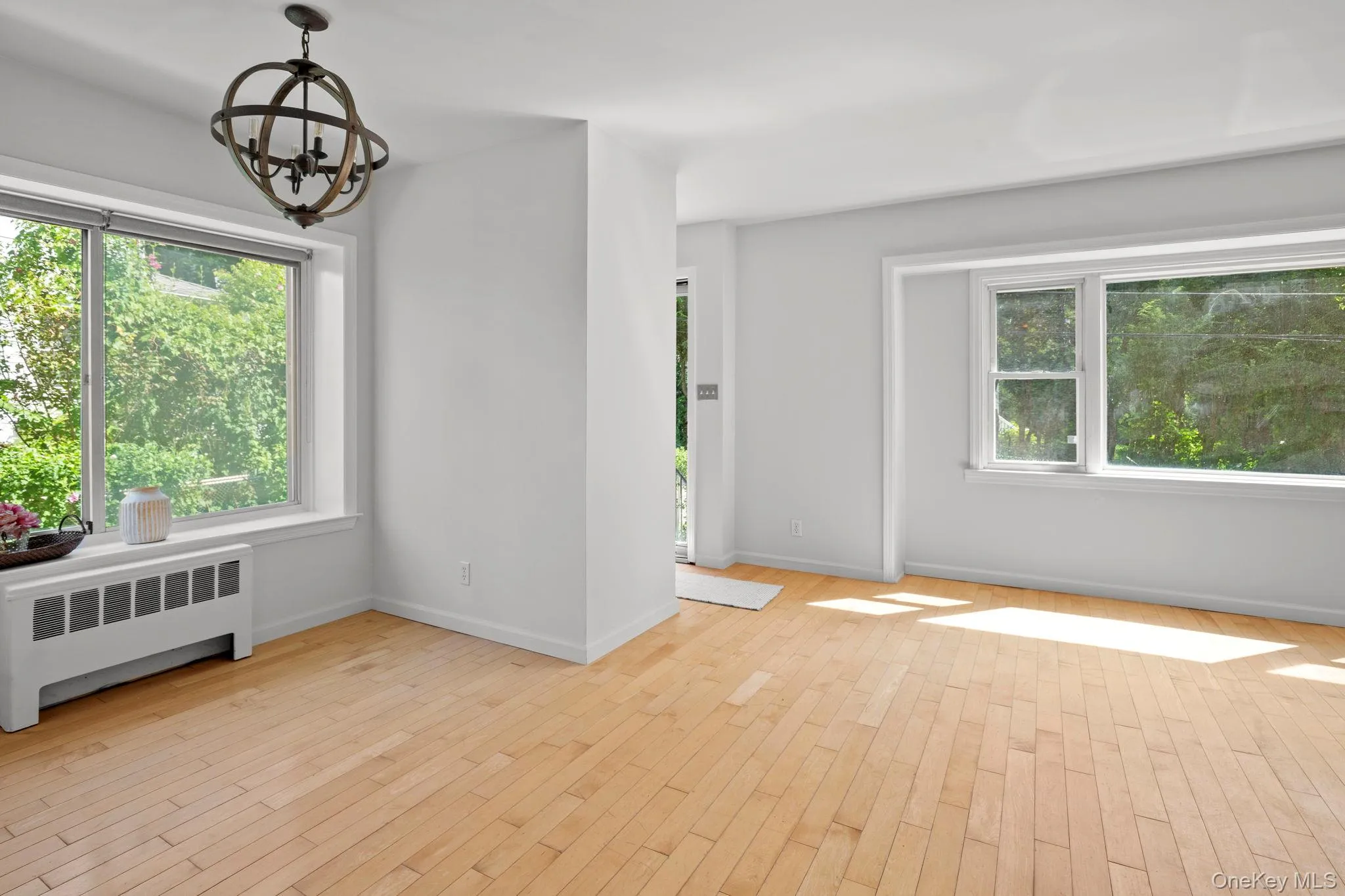 Spare room with radiator, a chandelier, wood finished floors, and healthy amount of natural light Spare room with radiator, a chandelier, wood finished floors, and healthy amount of natural light