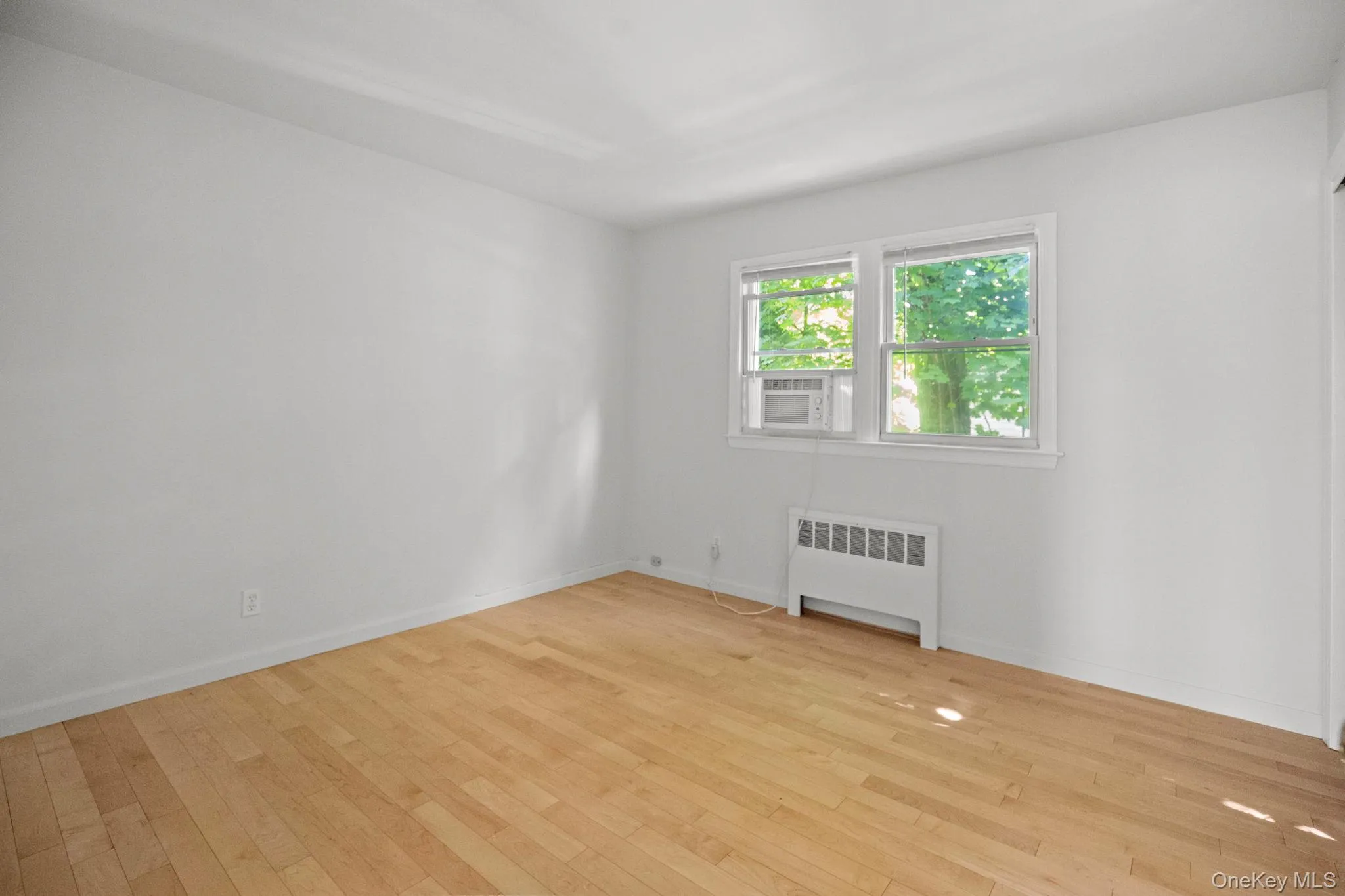 Spare room with light wood-type flooring, radiator, and cooling unit Spare room with light wood-type flooring, radiator, and cooling unit