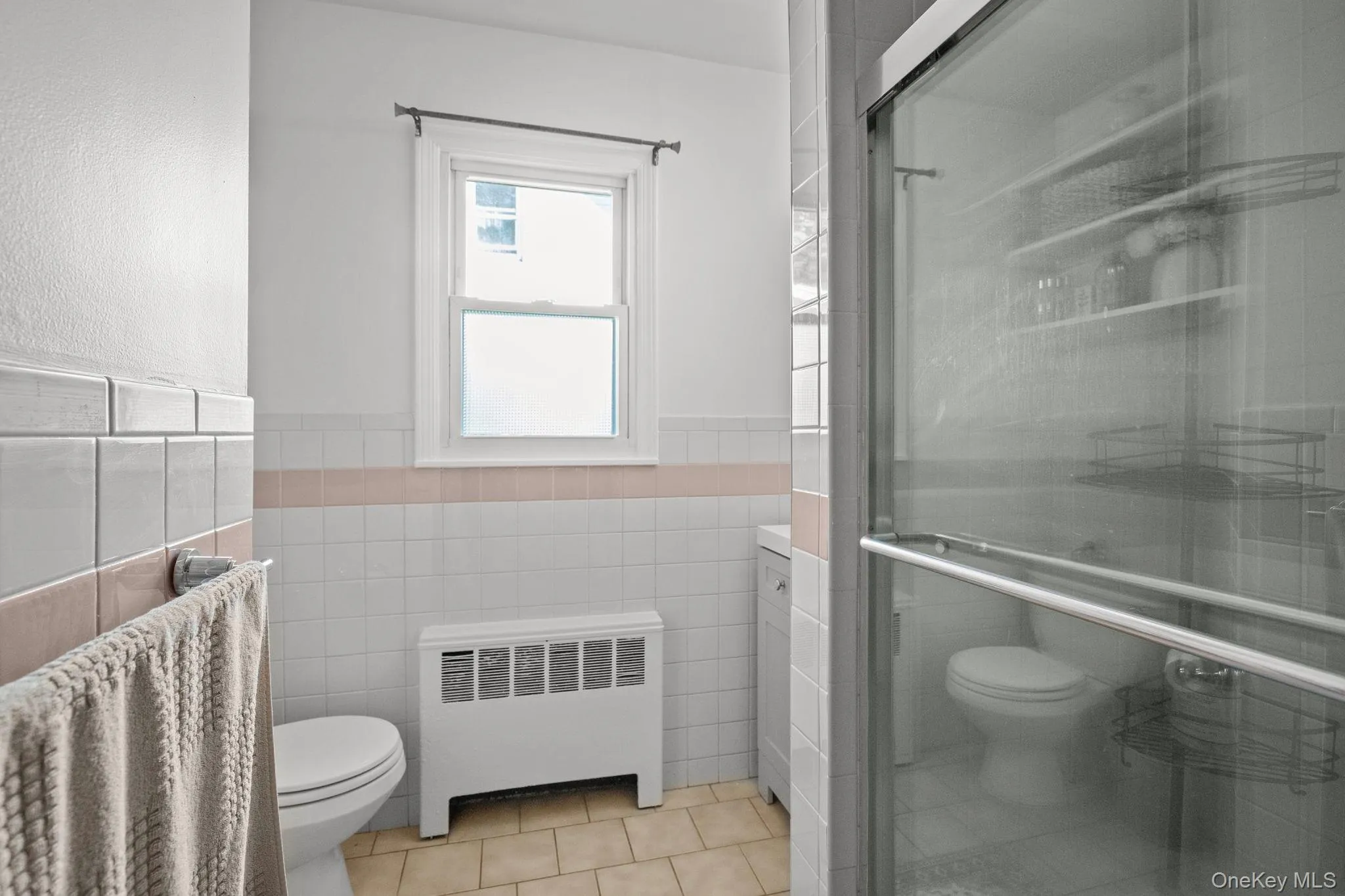 Full bath featuring radiator heating unit, tile patterned floors, a wainscoted wall, a shower stall, and tile walls Full bath featuring radiator heating unit, tile patterned floors, a wainscoted wall, a shower stall, and tile walls