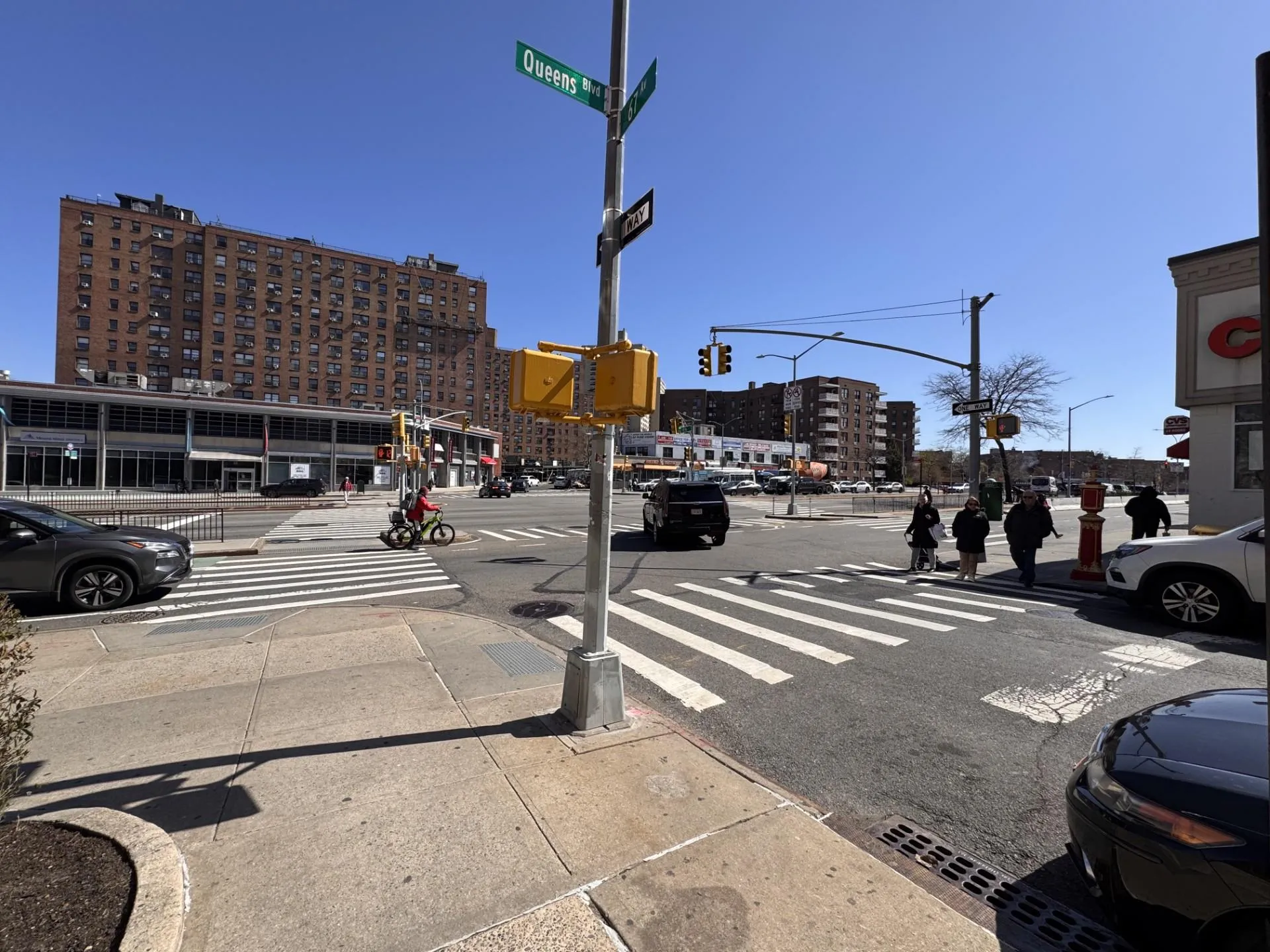 View of asphalt road with street lights, traffic lights, sidewalks, a city view, and curbs View of asphalt road with street lights, traffic lights, sidewalks, a city view, and curbs