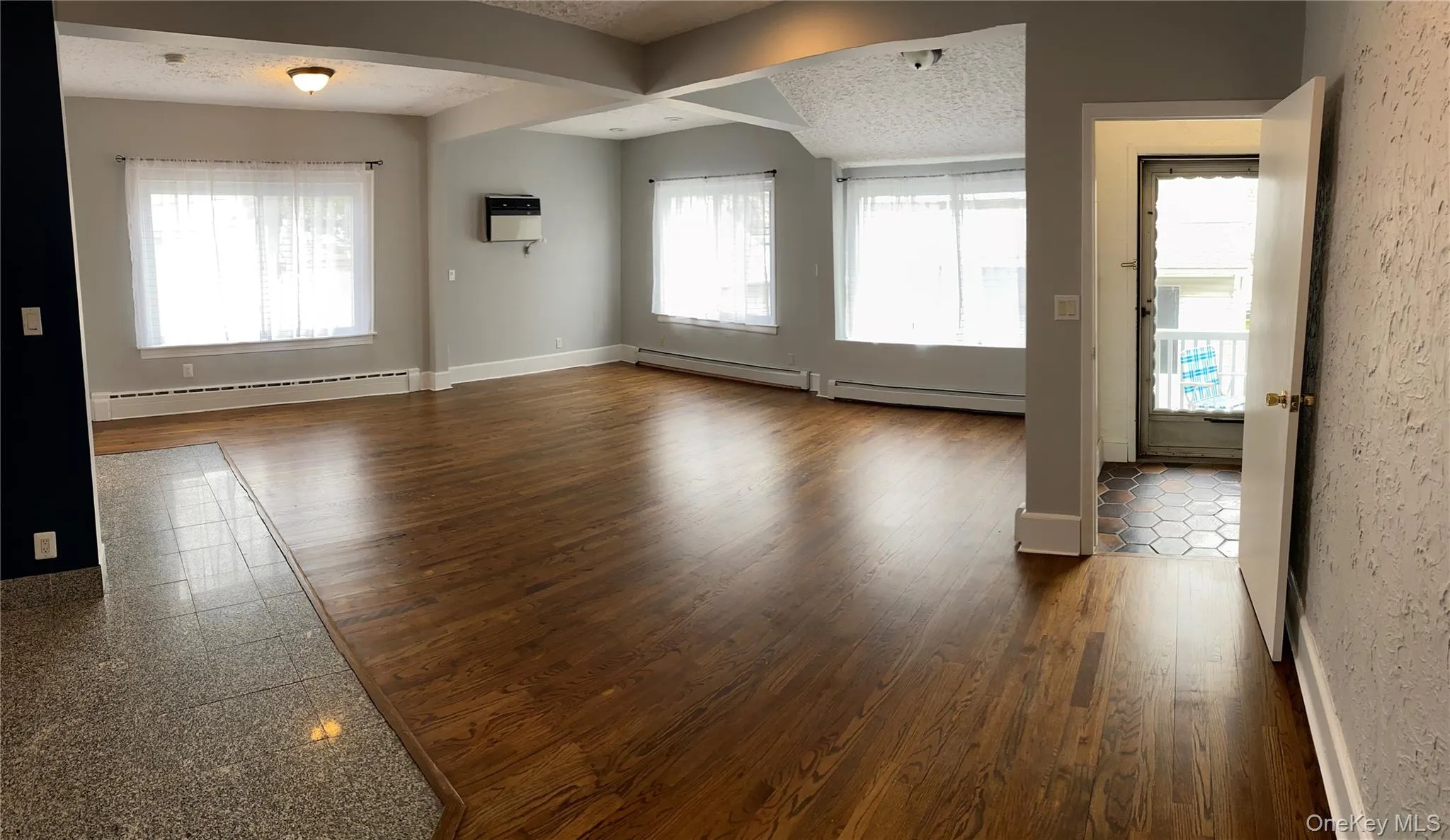 Spare room featuring a baseboard radiator, a textured ceiling, dark wood-style floors, and arched walkways Spare room featuring a baseboard radiator, a textured ceiling, dark wood-style floors, and arched walkways