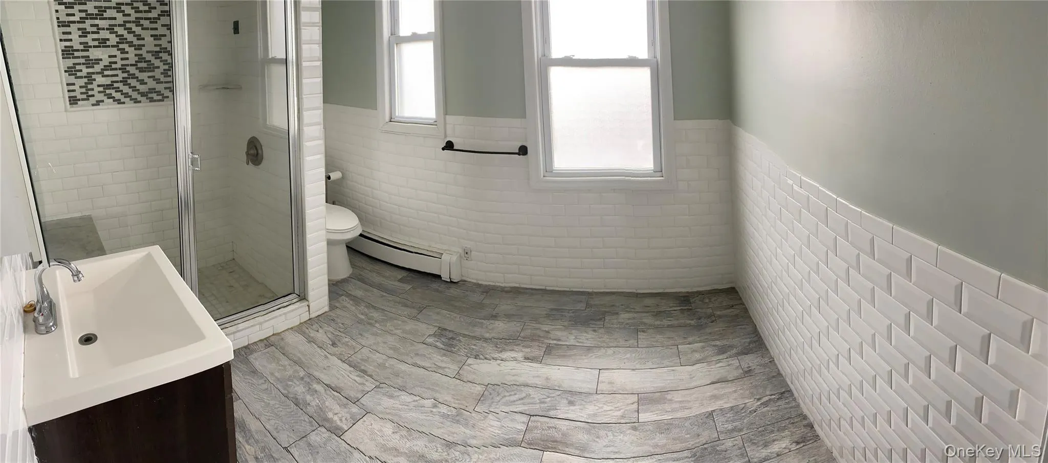 Full bathroom featuring tile walls, a wainscoted wall, plenty of natural light, a shower stall, and vanity Full bathroom featuring tile walls, a wainscoted wall, plenty of natural light, a shower stall, and vanity
