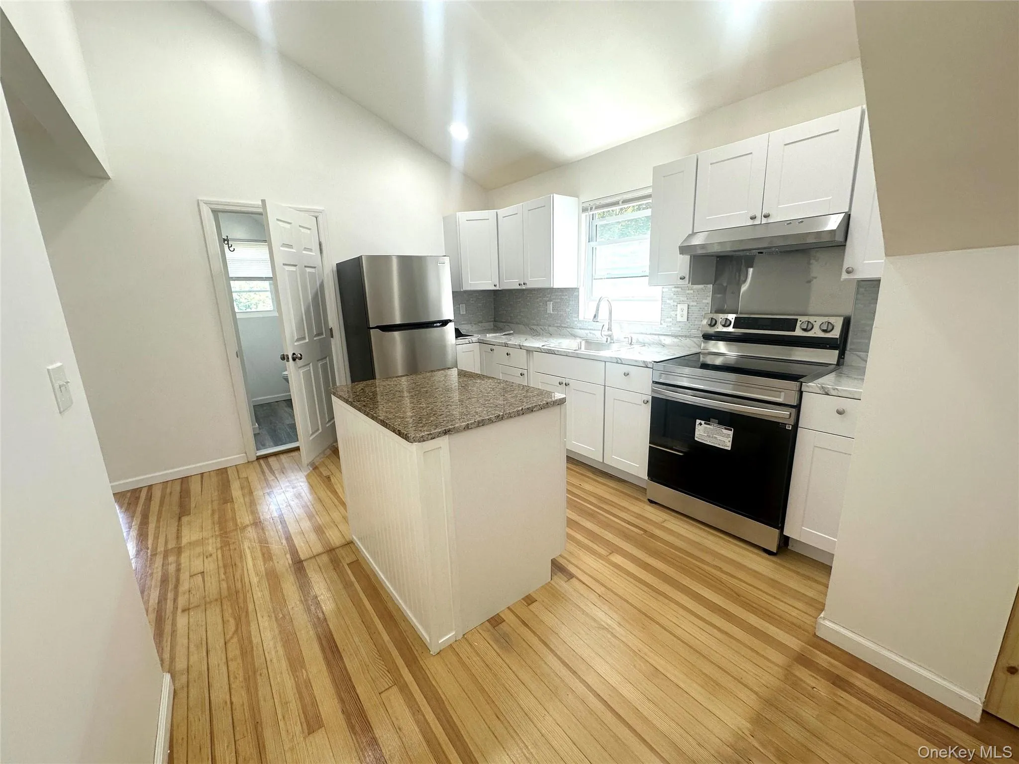 Kitchen featuring appliances with stainless steel finishes, a center island, white cabinetry, stone counters, and light wood-style flooring Kitchen featuring appliances with stainless steel finishes, a center island, white cabinetry, stone counters, and light wood-style flooring