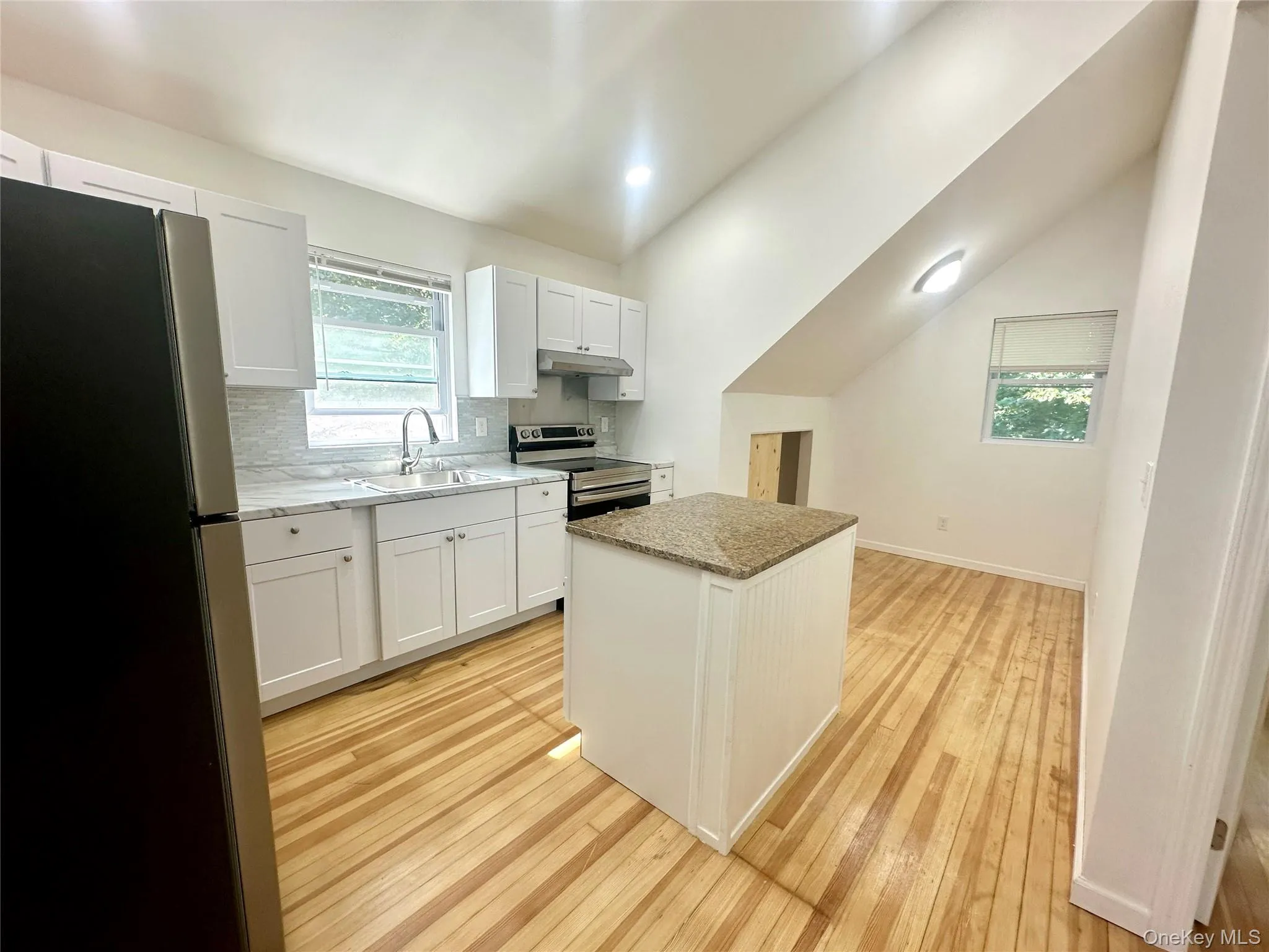 Kitchen with vaulted ceiling, appliances with stainless steel finishes, backsplash, a kitchen island, and white cabinets Kitchen with vaulted ceiling, appliances with stainless steel finishes, backsplash, a kitchen island, and white cabinets