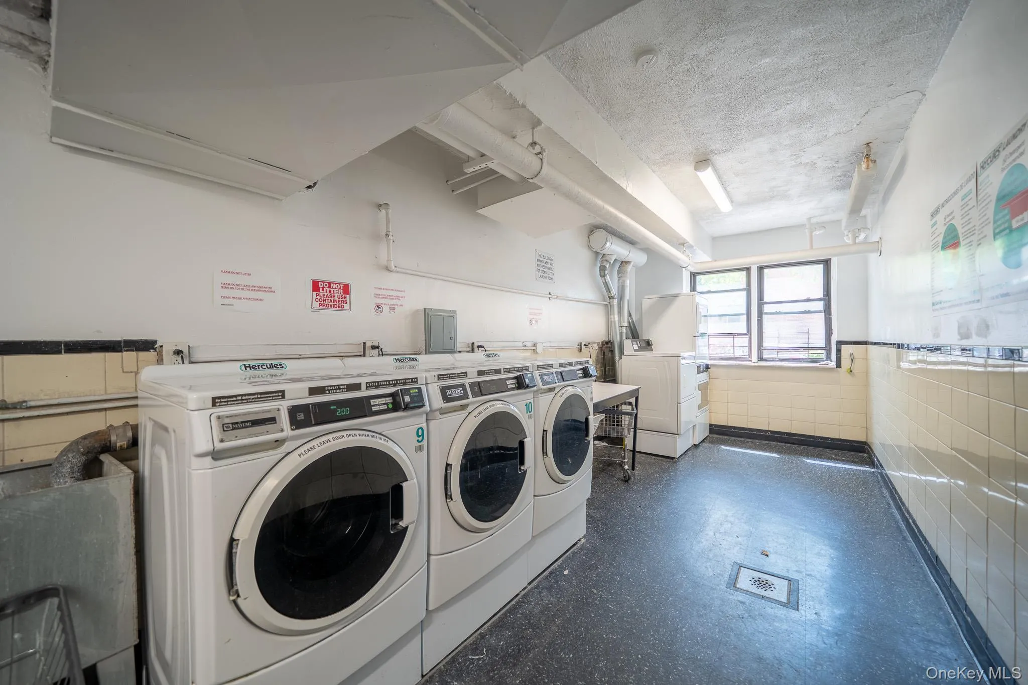 Community laundry room featuring washer and clothes dryer, a textured ceiling, a wainscoted wall, and tile walls Community laundry room featuring washer and clothes dryer, a textured ceiling, a wainscoted wall, and tile walls
