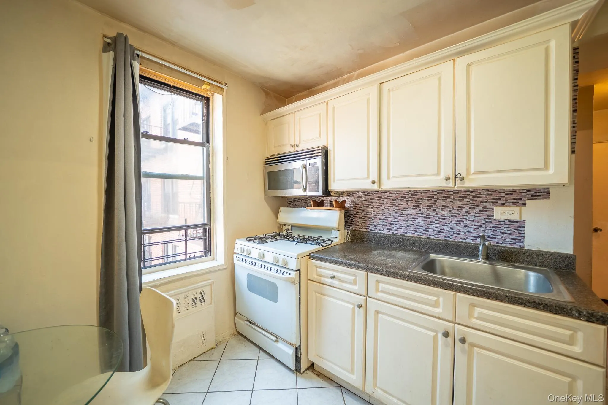 Kitchen with white range with gas stovetop, stainless steel microwave, dark countertops, and backsplash Kitchen with white range with gas stovetop, stainless steel microwave, dark countertops, and backsplash
